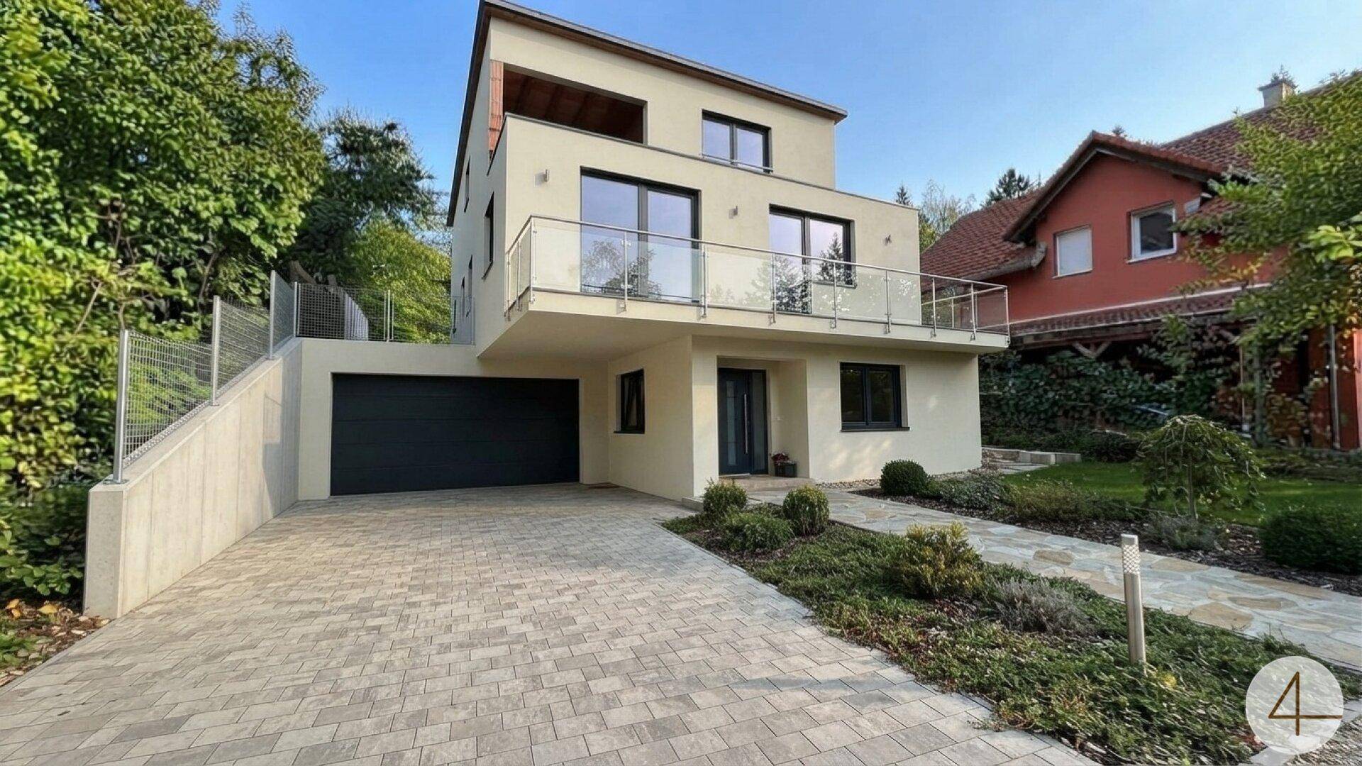 Fertiggestelltes modernes Einfamilienhaus mit heller Fassade, Balkon und gepflasterter Auffahrt.