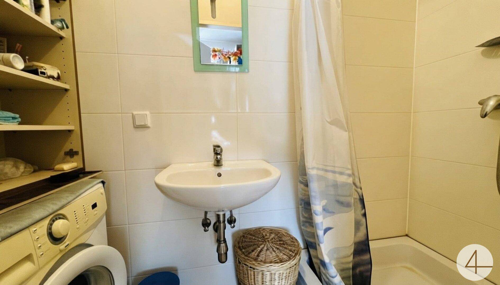 Funktionales Badezimmer mit Waschbecken, Spiegel, Badewanne mit Duschvorhang und Waschmaschine.