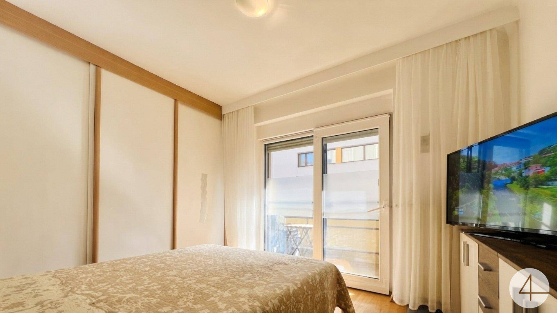 Gemütliches Schlafzimmer mit Zugang zu einem kleinen Balkon und einem Fernseher.