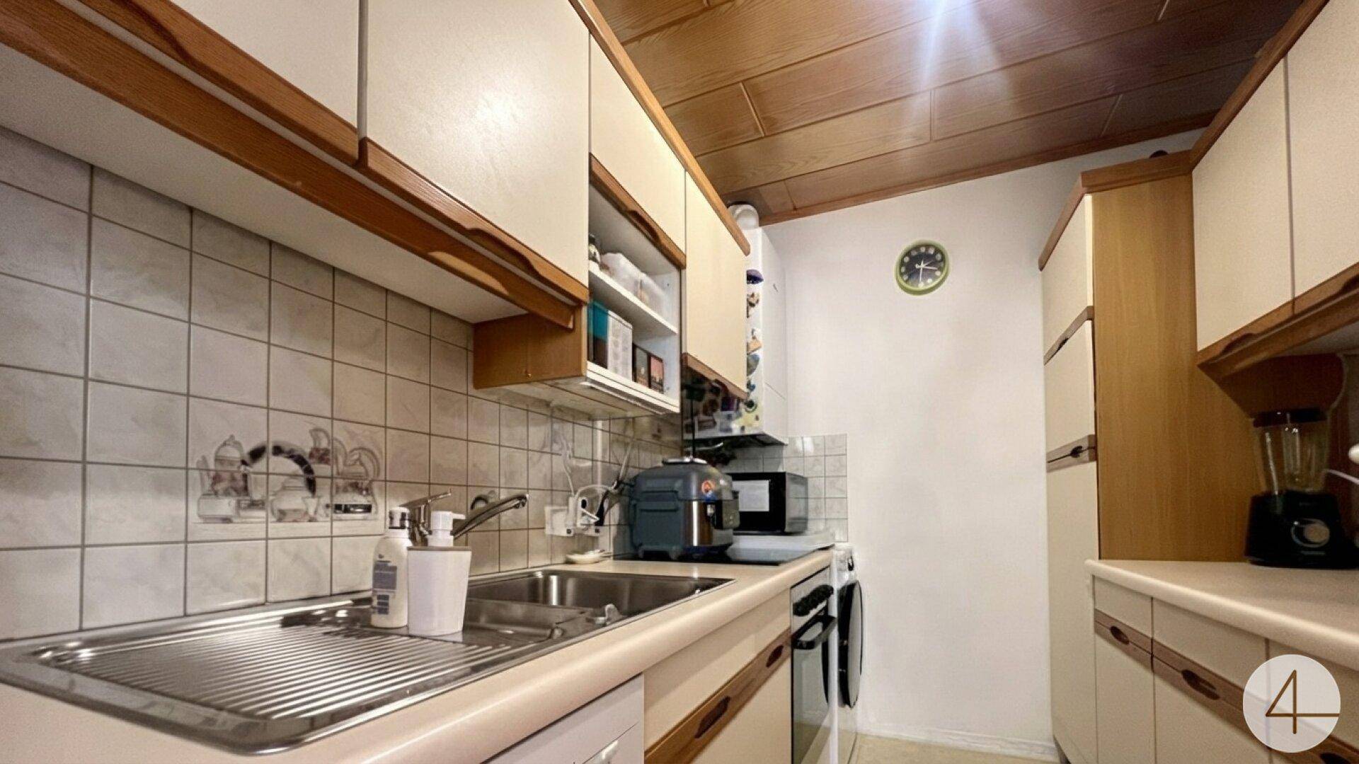 Funktionale Küche mit beigen Schränken, Fliesenrückwand und Holzdecke.