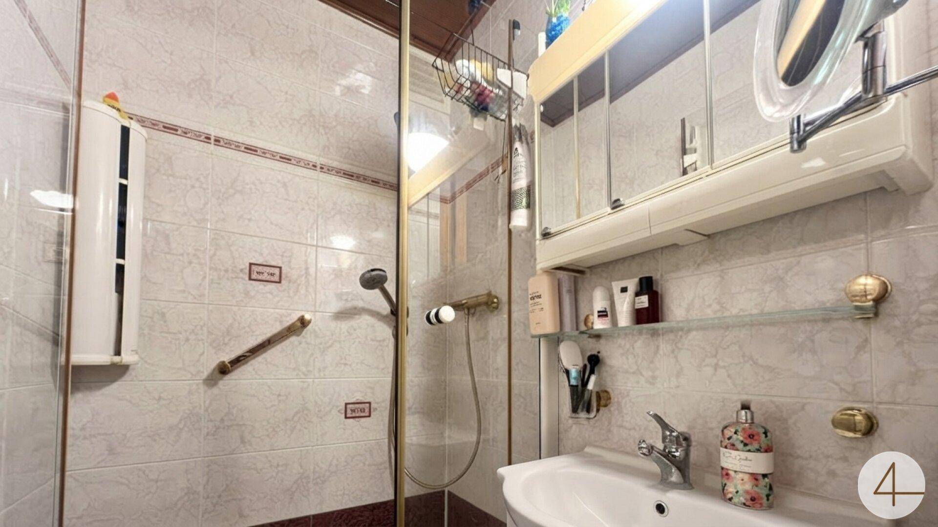 Gefliestes Badezimmer mit Duschkabine, Waschbecken und Spiegelschrank.