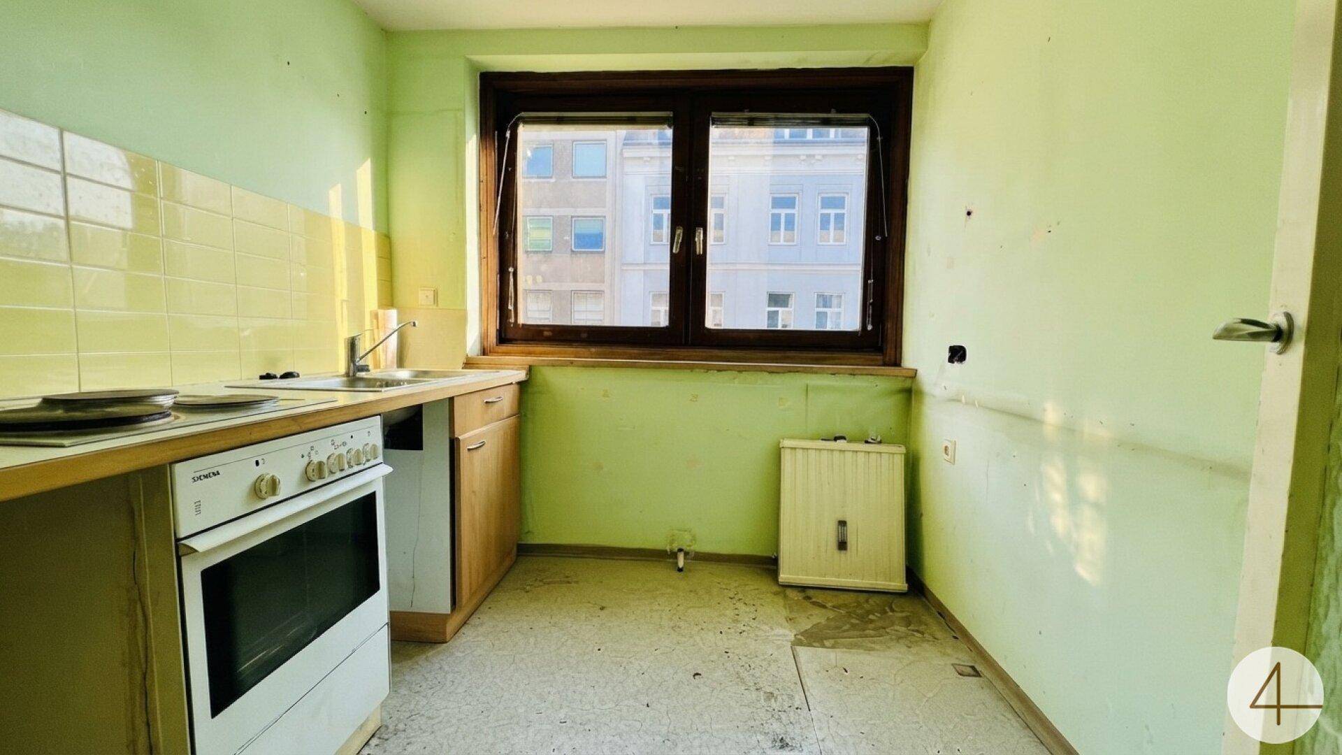 Einfache Küche mit grün gestrichenen Wänden, Spüle, Herd und einem Fenster mit Stadtblick.