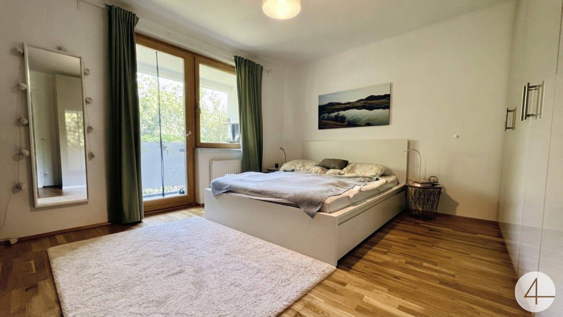 Geräumiges Schlafzimmer mit Doppelbett, Parkettboden und Zugang zum Balkon.