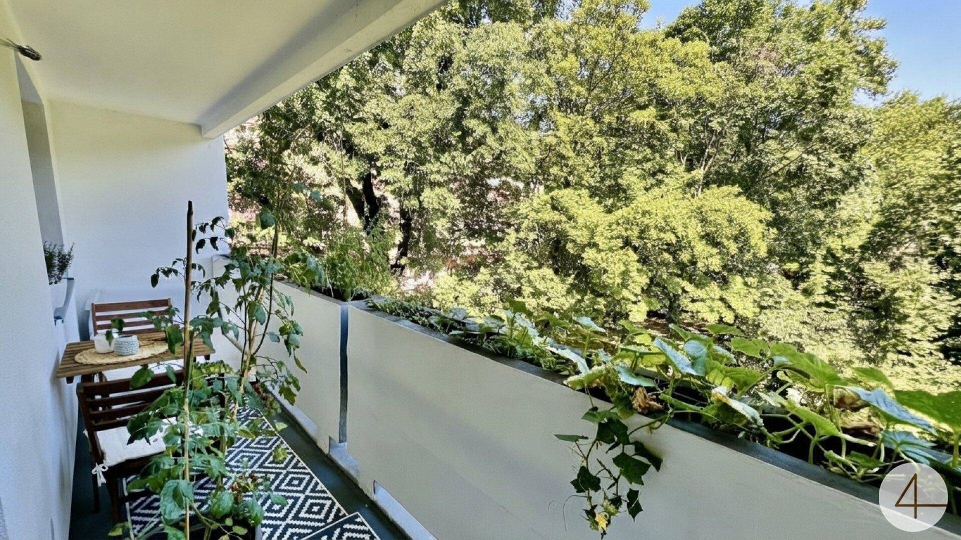 Schmaler Balkon mit Pflanzen und Sitzgelegenheiten, umgeben von viel Grün.