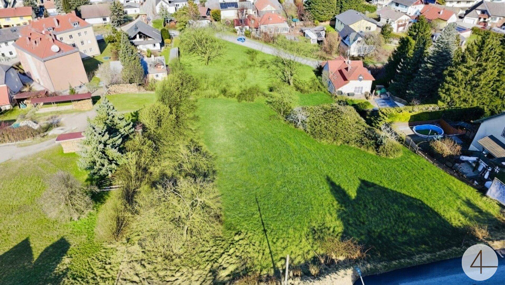 Weitläufiges grünes Grundstück aus der Vogelperspektive, umgeben von Wohnbebauung und Natur.