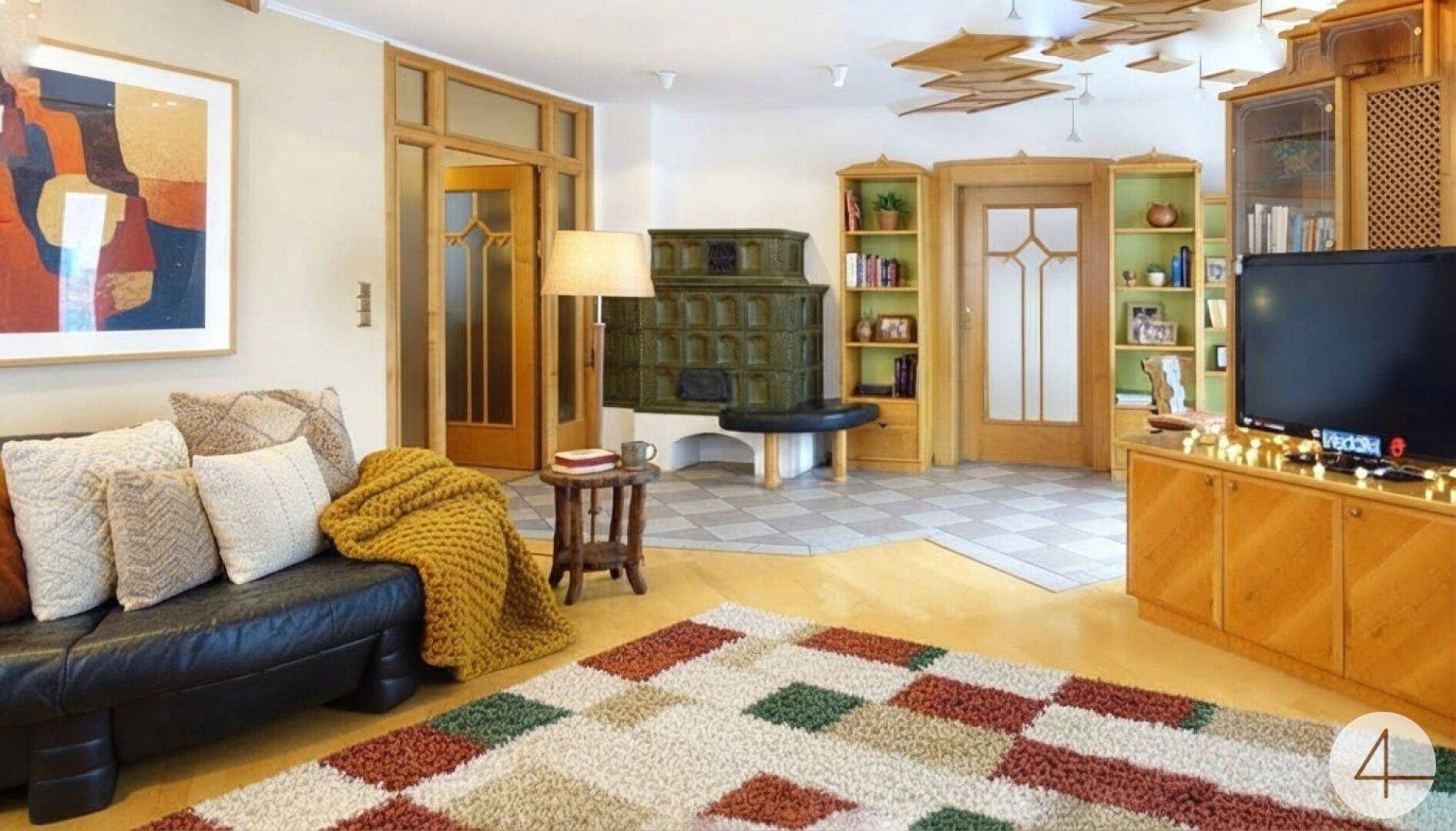 Gemütliches Wohnzimmer mit Kachelofen, Holzböden und einem bunten Teppich, sehr einladend.