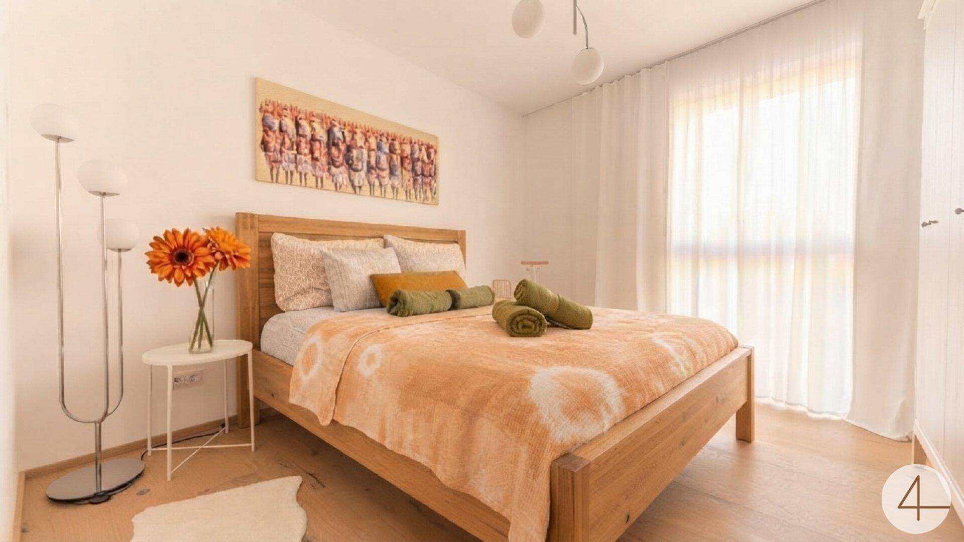 Helles Schlafzimmer mit Holzbett, Holzboden und großen Fenstern für viel Tageslicht.
