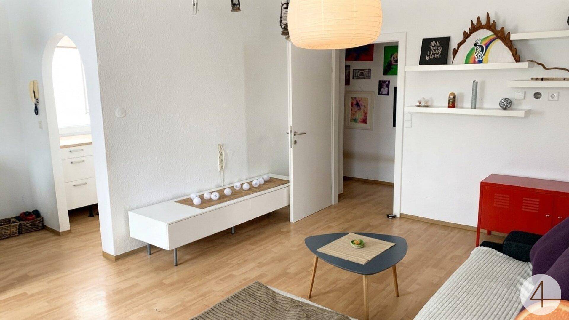Gemütliches Wohnzimmer mit Holzboden, weiß gestrichenen Wänden und einem Bogen zu einem Nebenraum.