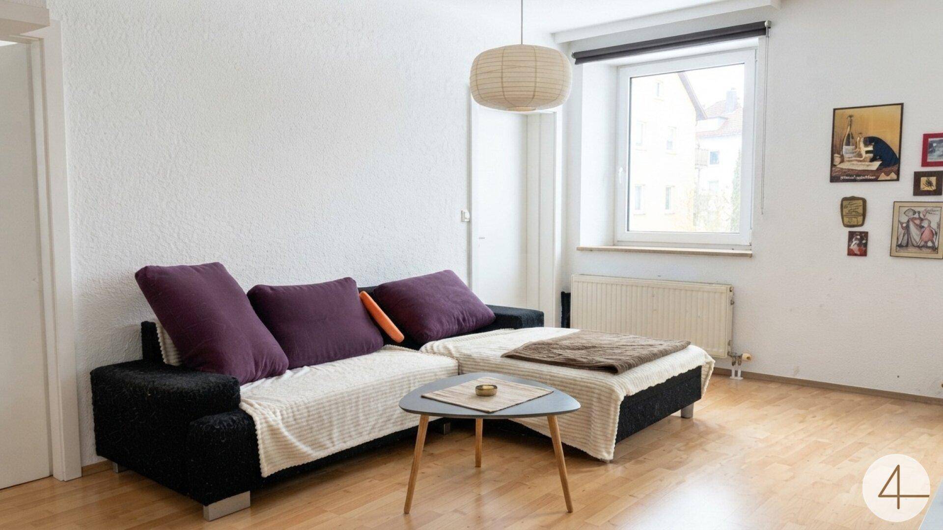 Wohnzimmer mit bequemer Couch, Couchtisch und einem Fenster, das viel Tageslicht hereinlässt.
