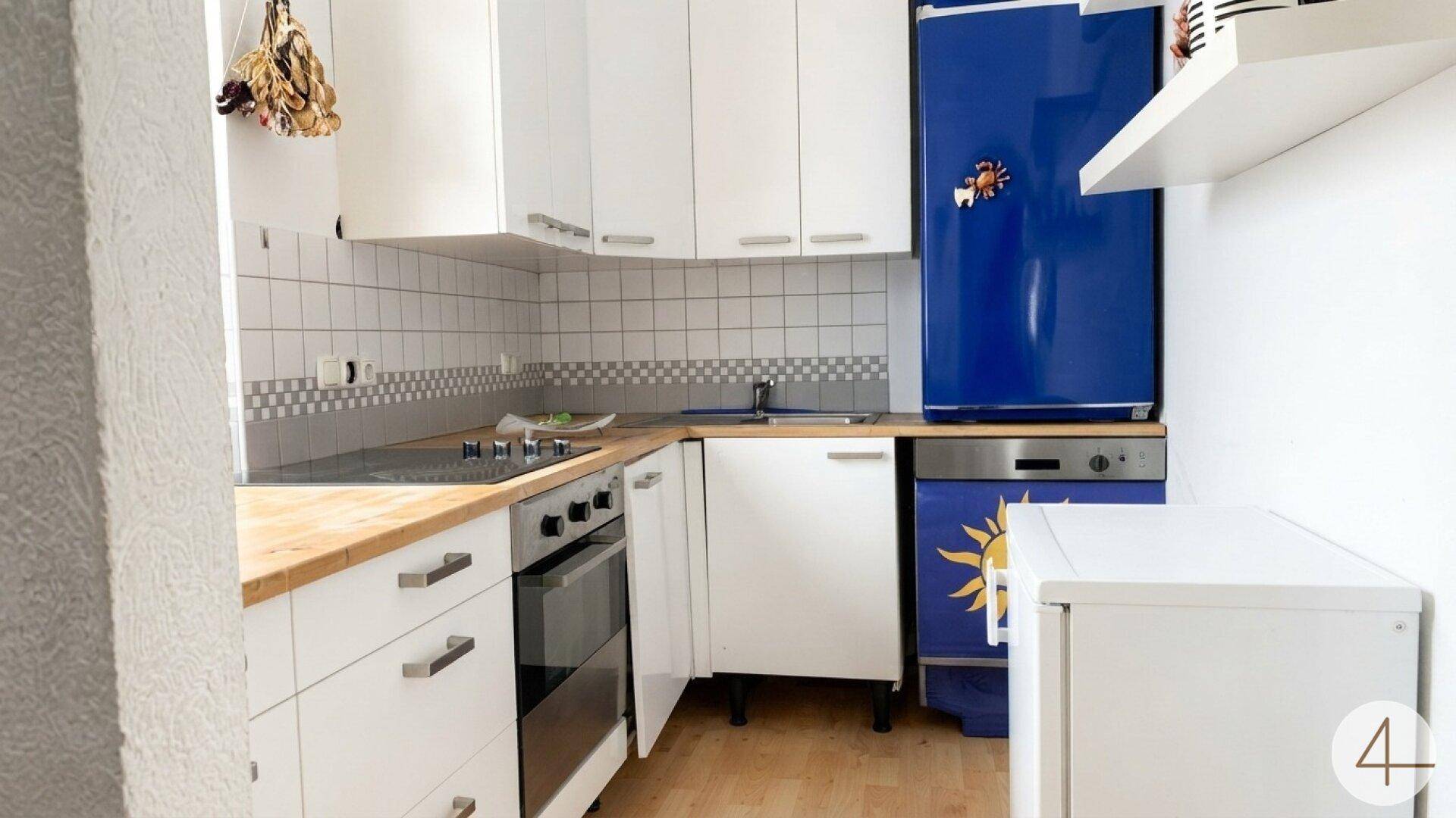 Funktionale Küche mit weißen Schränken, Holzarbeitsplatte und auffälligen blauen Geräten.