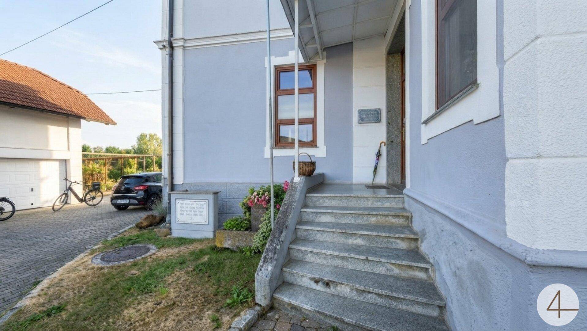Eingangsbereich des Gebäudes mit Steintreppe, überdachtem Zugang und einem gepflegten Vorgarten.