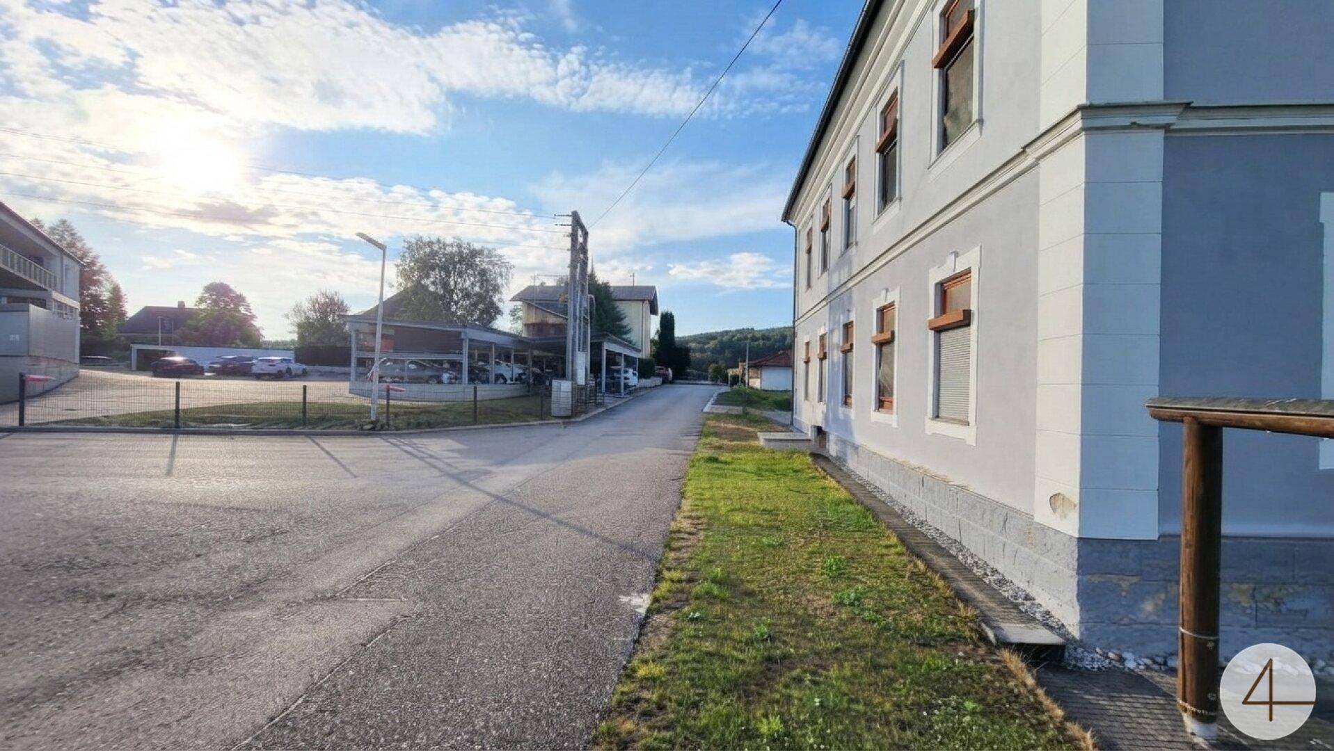 Blick auf die ruhige Straße neben dem Gebäude mit Parkplätzen und umliegender ländlicher Bebauung.