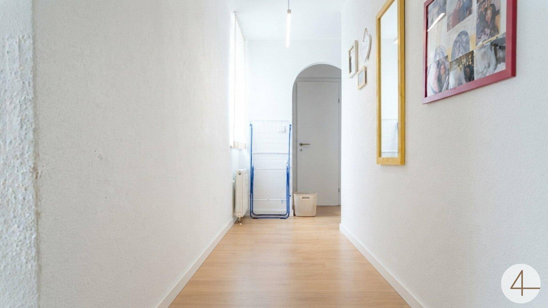 Heller Flur mit Holzboden, weißen Wänden und einem eleganten Bogen, der zu weiteren Räumen führt.