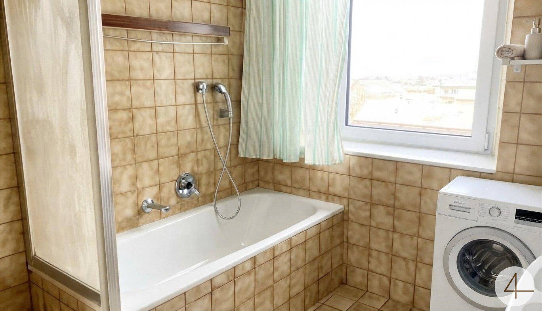 Badezimmer mit Badewanne, Duschvorrichtung und Waschmaschine, gefliest in warmen Brauntönen.