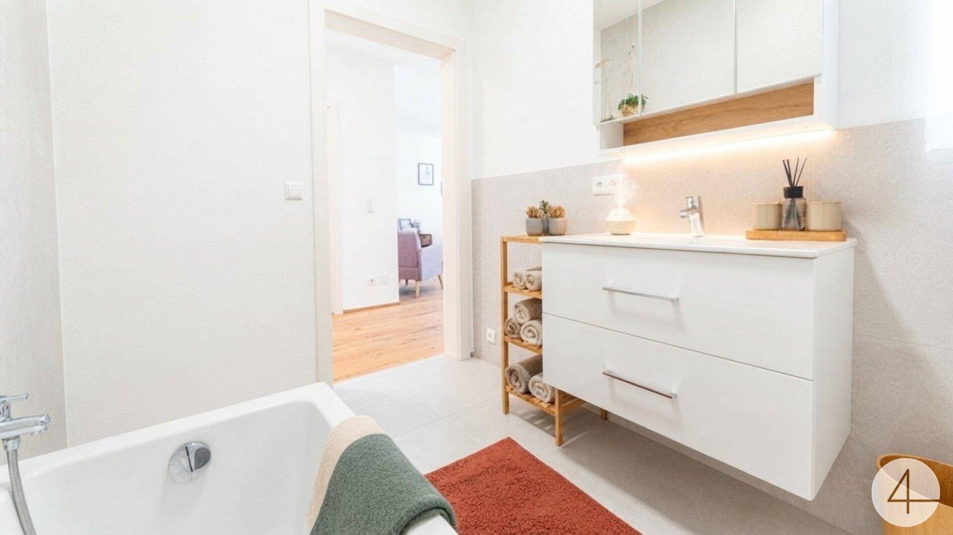 Modernes Badezimmer mit Badewanne, Waschtischunterschrank und beleuchtetem Spiegelschrank.
