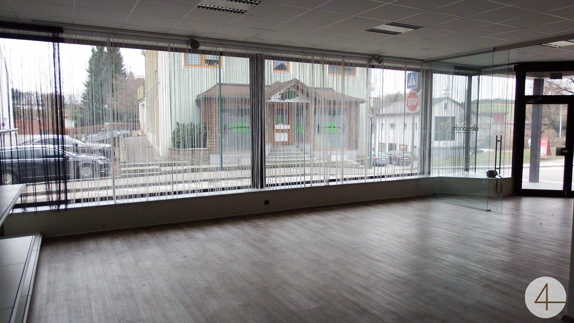 Großer, leerer Raum mit bodentiefen Fenstern und Blick auf die Straße.