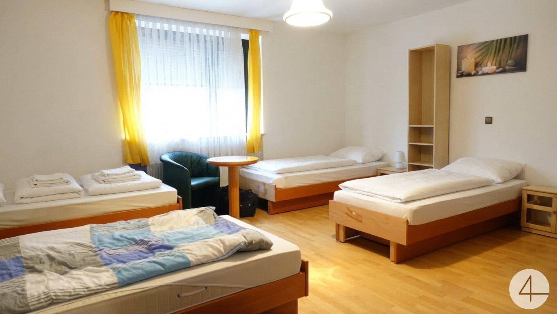 Helles Schlafzimmer mit mehreren Einzelbetten, Holzfußboden und gelben Vorhängen.