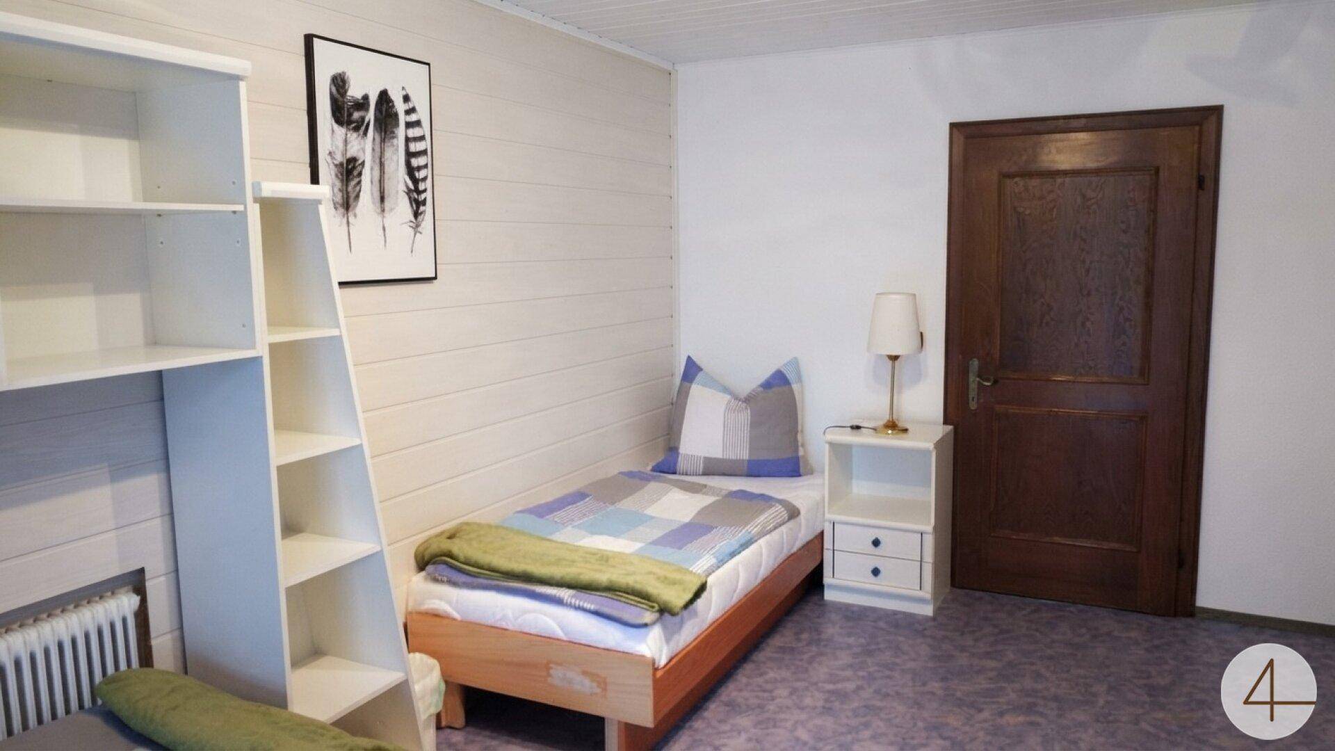 Gemütliches Schlafzimmer mit Einzelbett, weißem Regal und Holztür.