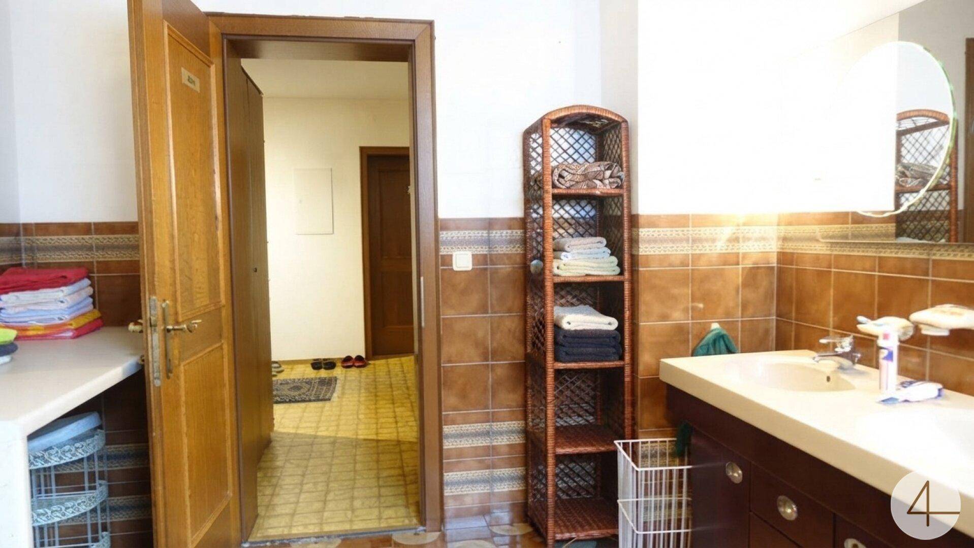 Badezimmer mit braunen Fliesen, Waschbecken und einem runden Spiegel.