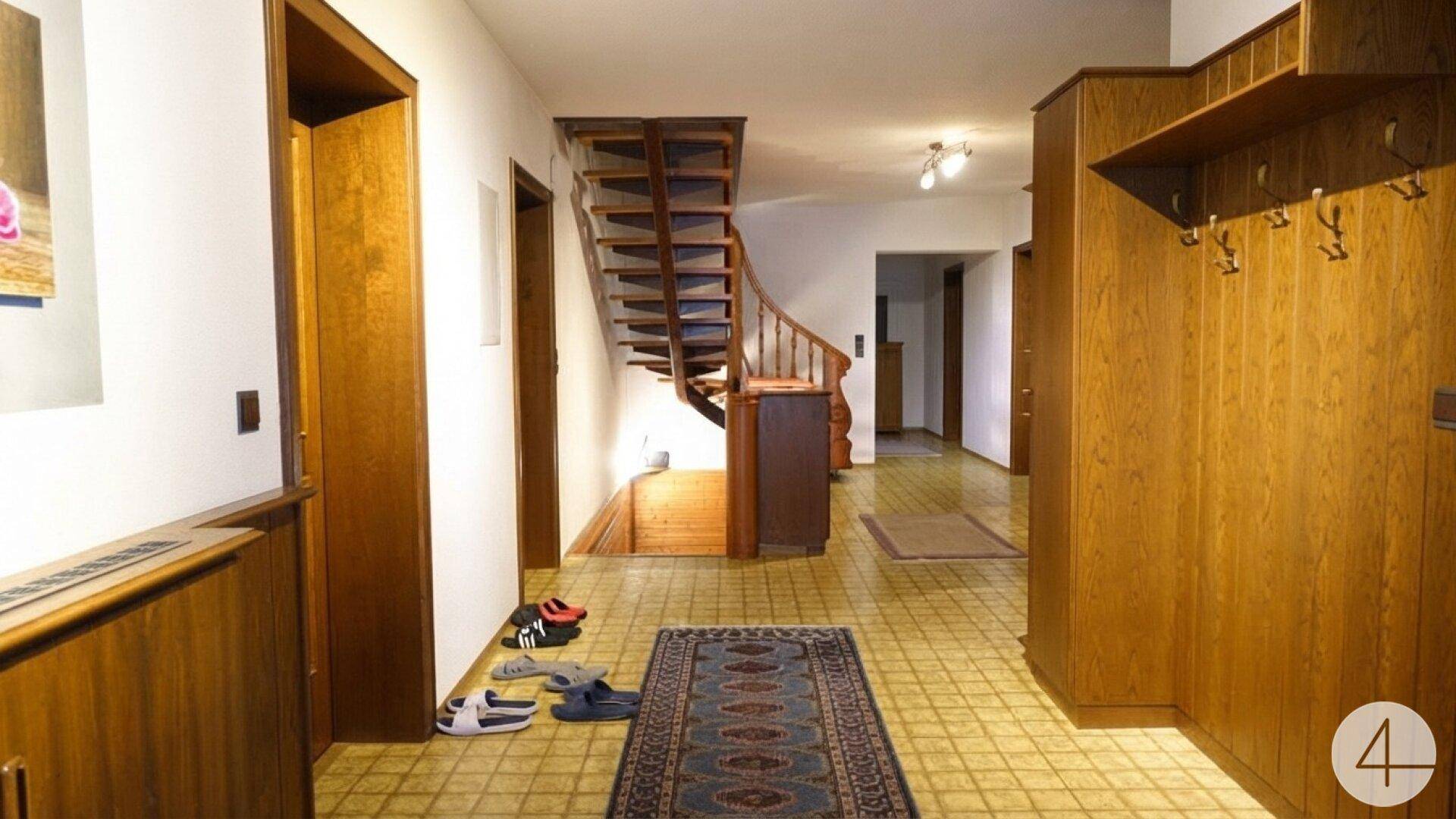 Geräumiger Flur mit Holztreppe, Garderobe und gemustertem Fliesenboden.