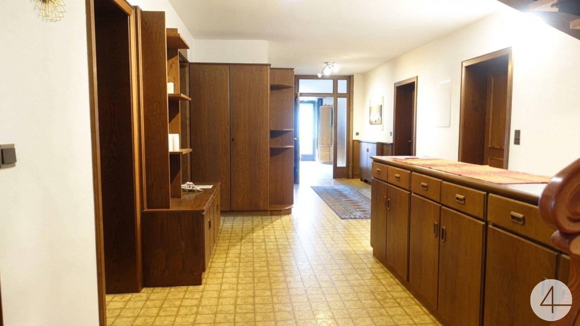 Langer Flur mit vielen Holzschränken und einem gemusterten Fliesenboden.