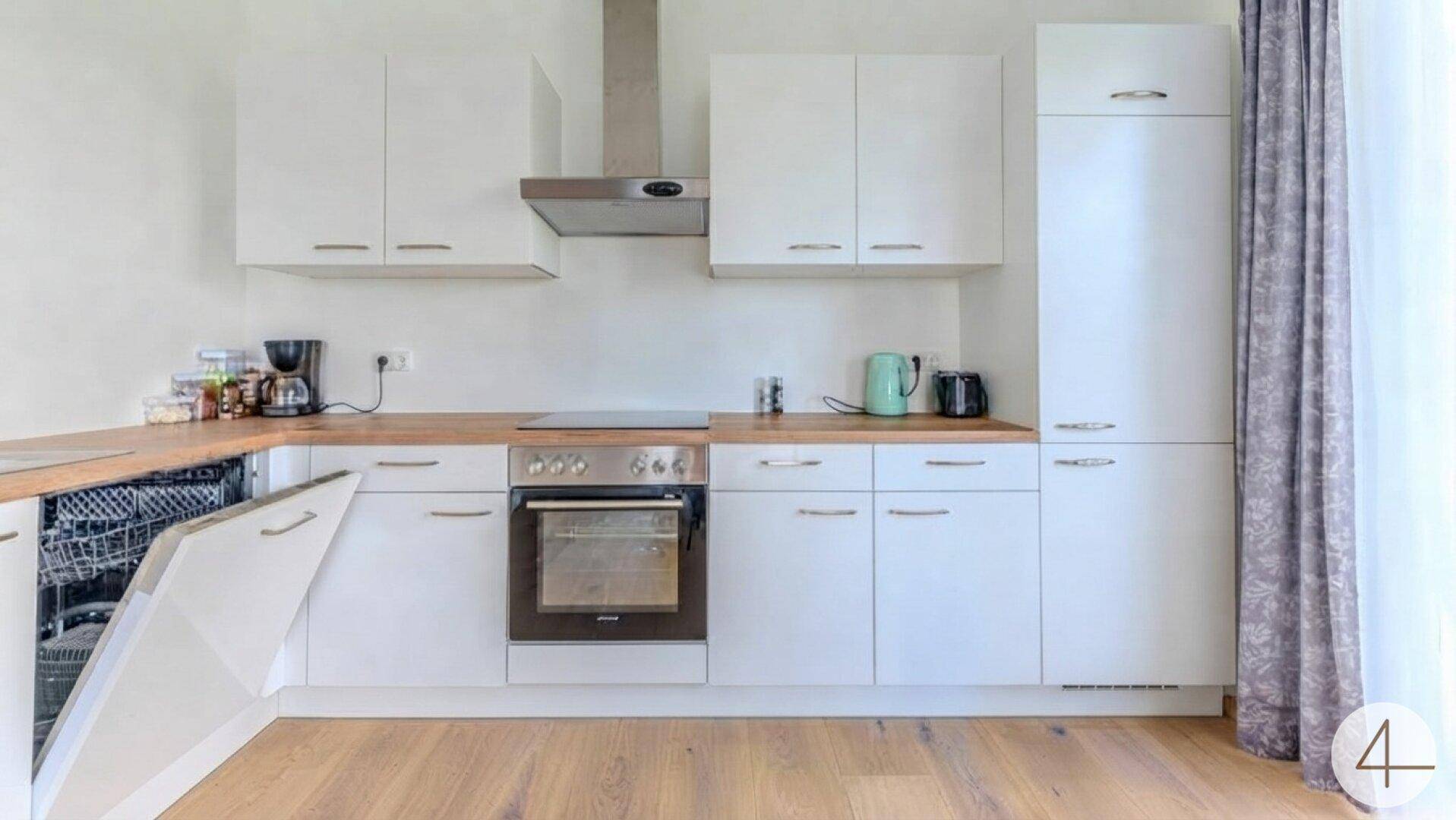 Helle Küche mit weißen Schränken, Holz-Arbeitsplatte und integrierten Geräten, inklusive Geschirrspüler und Backofen.