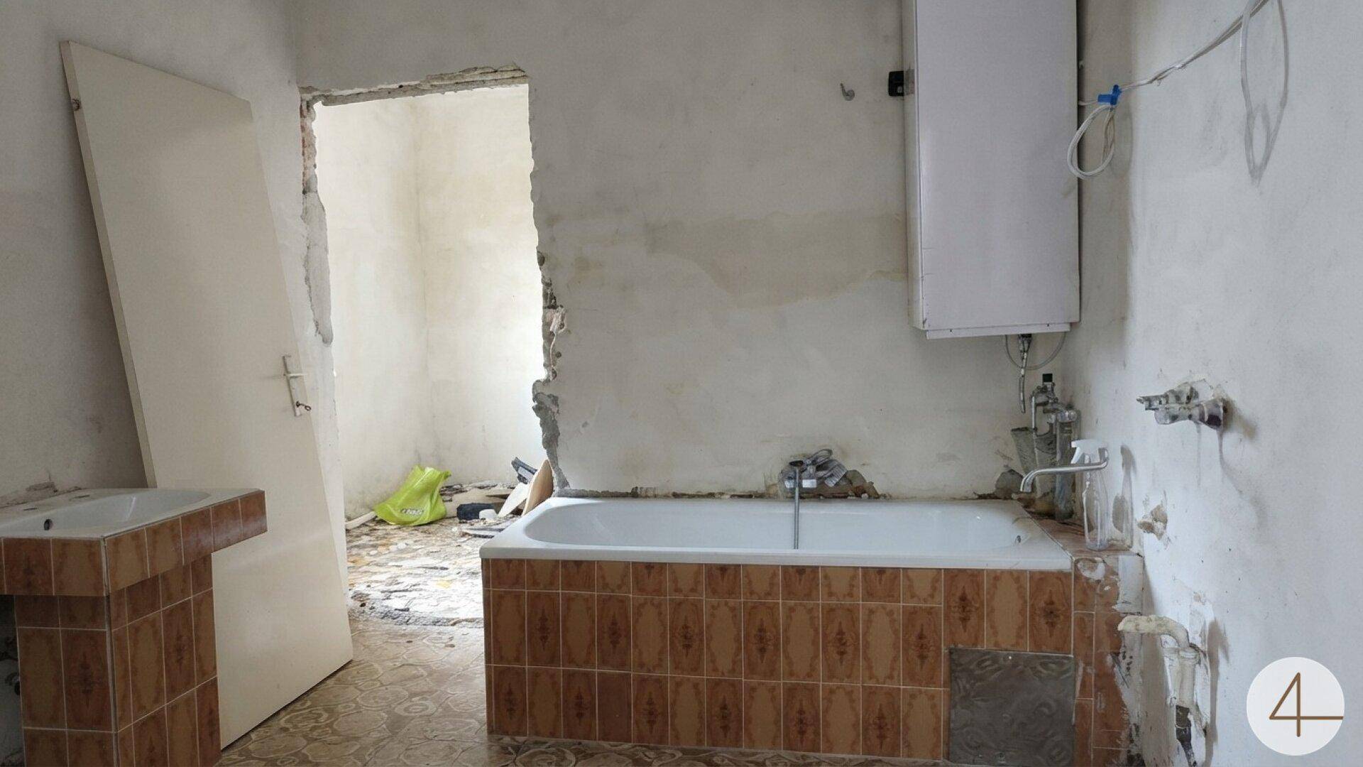 Badezimmer in Renovierung mit alter Badewanne, Waschbecken und unverputzten Wänden, die auf Sanierungsbedarf hinweisen.