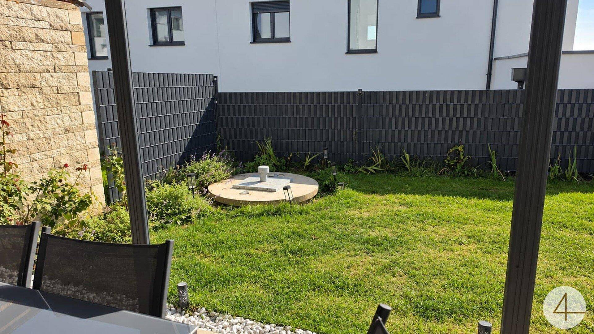 Blick auf den gepflegten Gartenbereich mit Rasenfläche und moderner Zaunanlage hinter dem Haus.