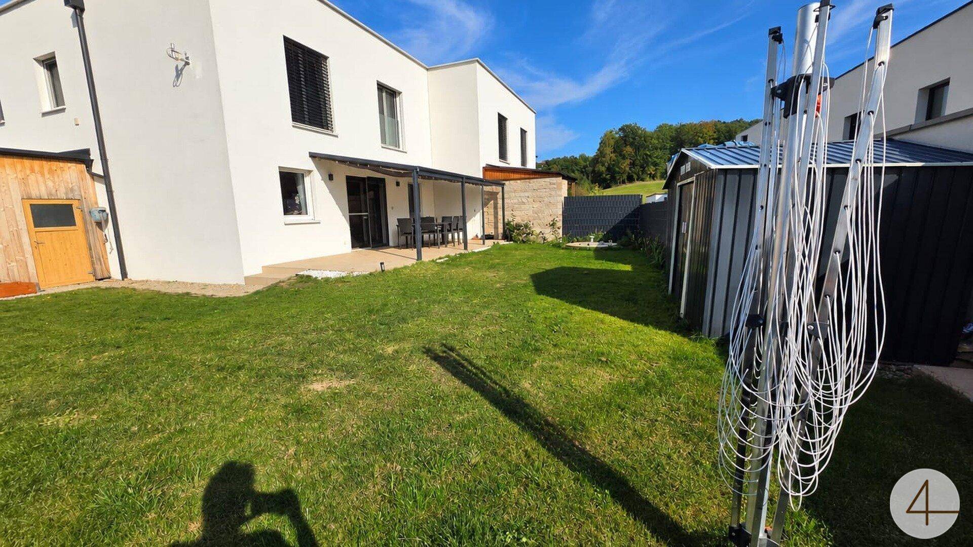 Weitläufiger Gartenbereich hinter dem modernen Haus mit Terrasse, Geräteschuppen und Wäschespinne.