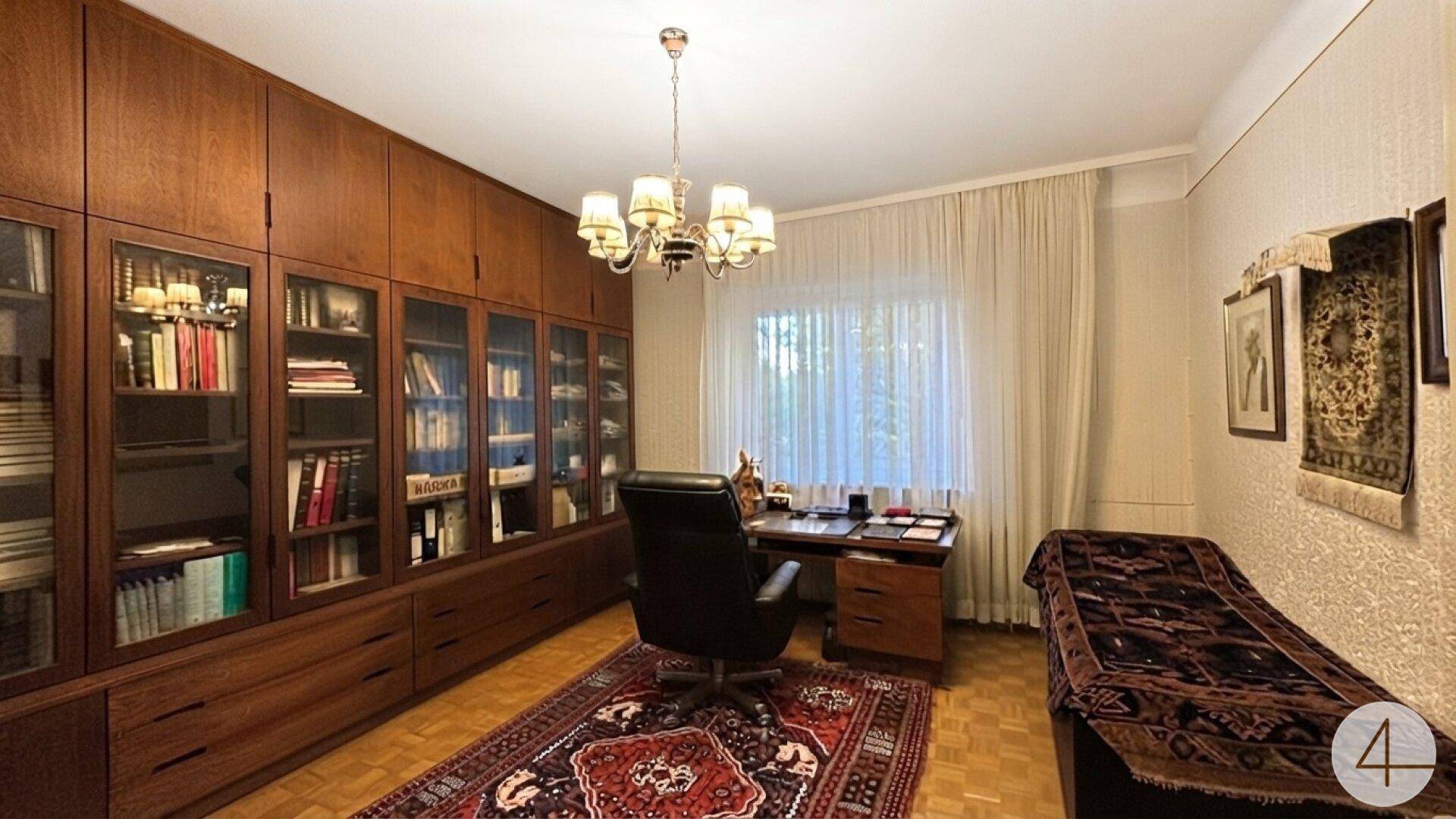 Klassisches Arbeitszimmer mit umfangreichen Holzregalen, Schreibtisch und Teppich.