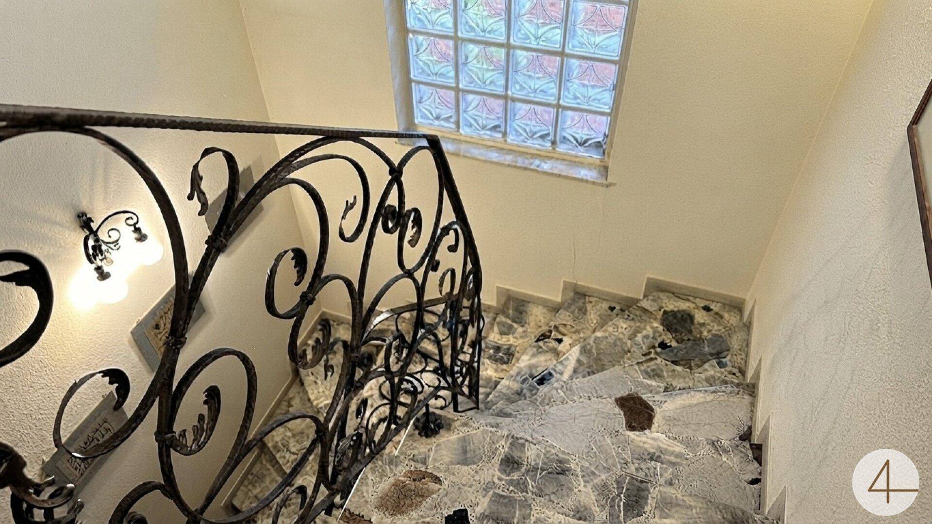 Blick von oben auf das Treppenhaus mit kunstvollem Geländer und Steinverkleidung.