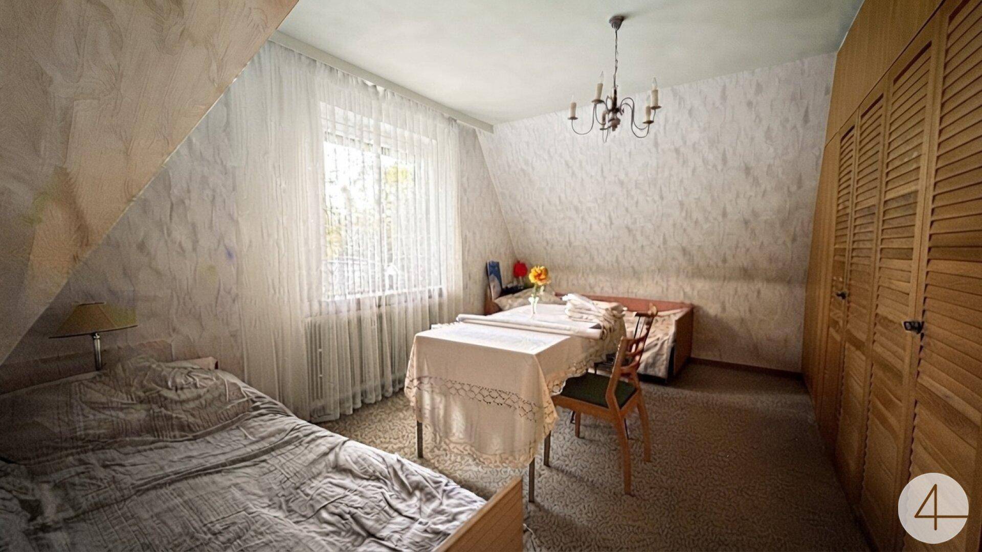 Schlafzimmer im Dachgeschoss mit schrägen Wänden, Teppichboden und Holzschränken.