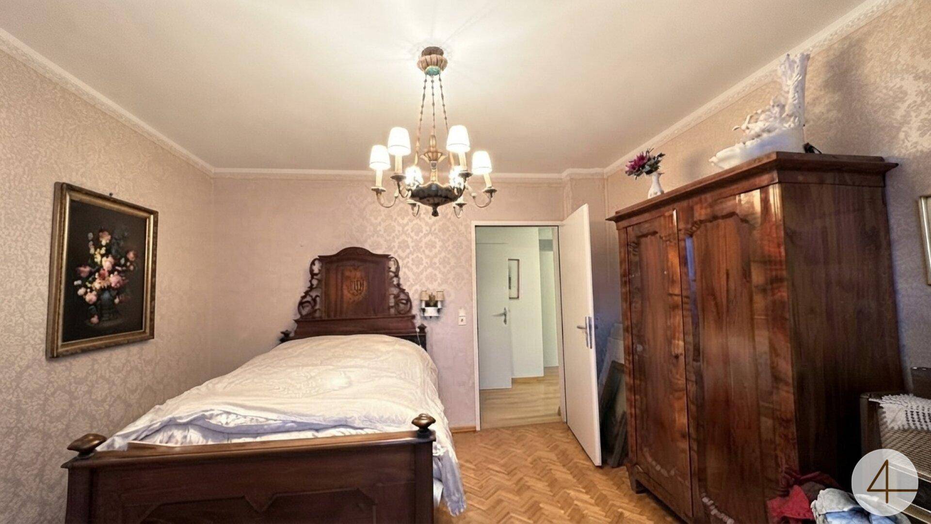 Geräumiges Schlafzimmer mit antikem Holzbett, Parkettboden und Kronleuchter.