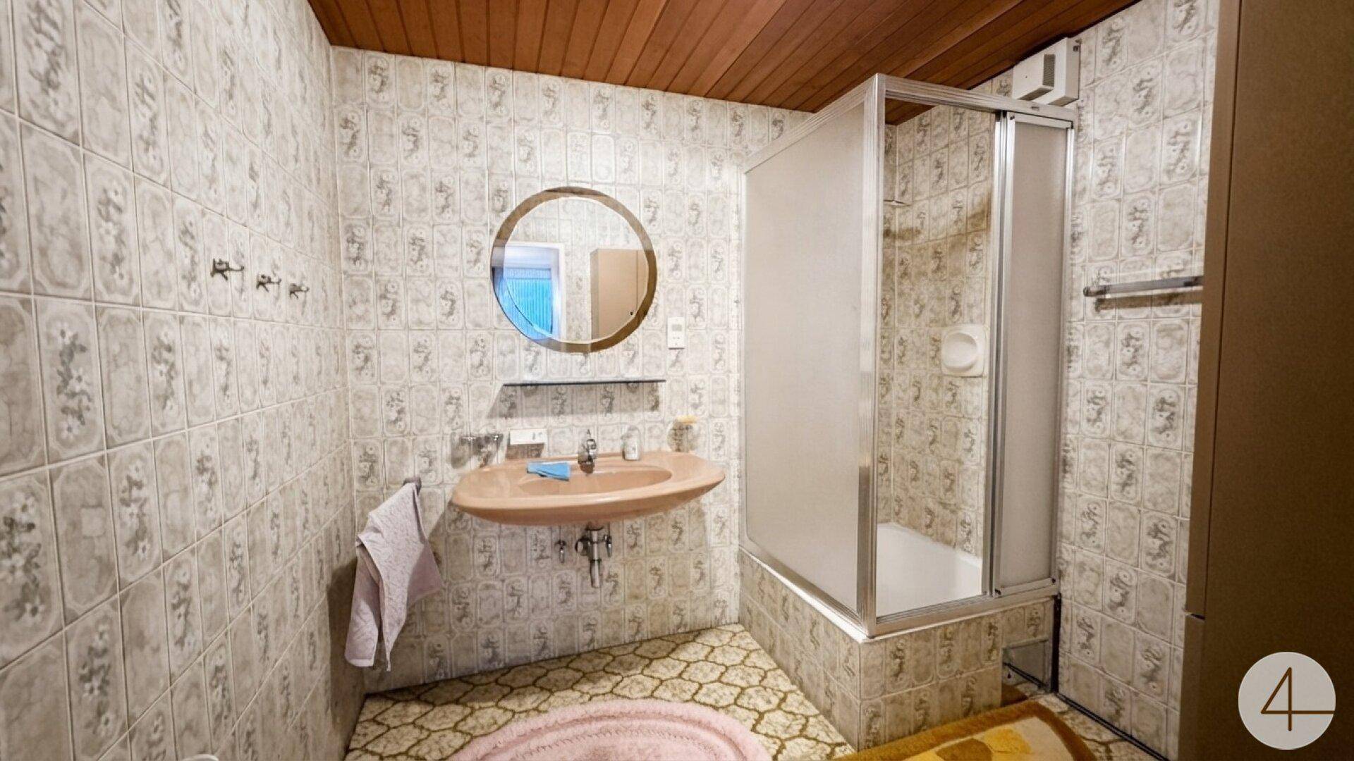 Badezimmer mit Duschkabine, Waschbecken und gemusterten Fliesen im 80er-Jahre-Stil.