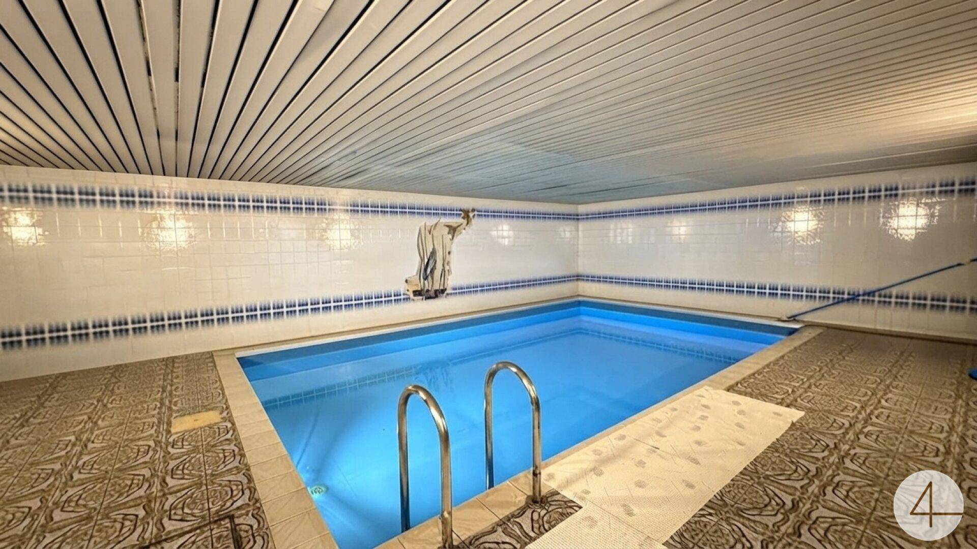 Innenpoolbereich mit gefliestem Becken und blauer Auskleidung für Entspannung und Sport.