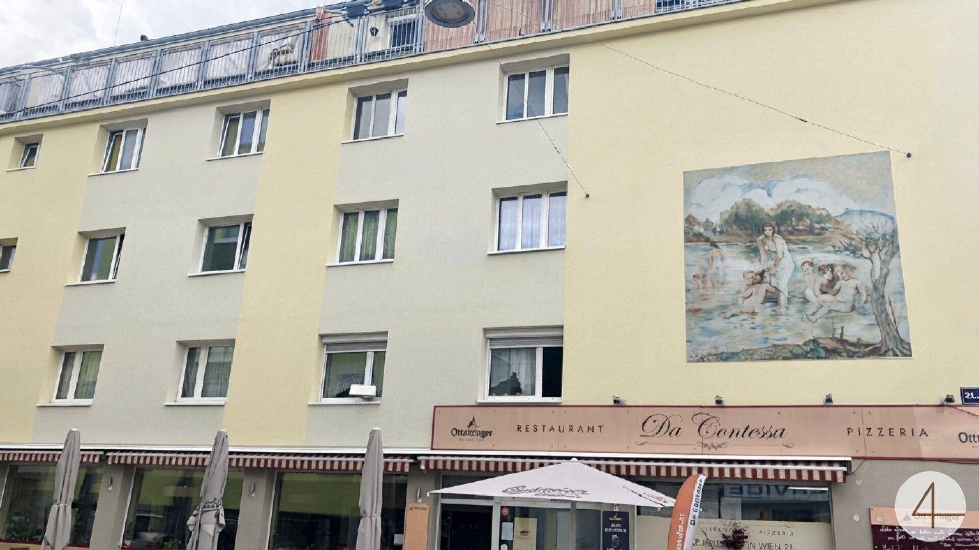 Fassade eines Wohngebäudes mit Geschäften im Erdgeschoss und einem Wandgemälde.