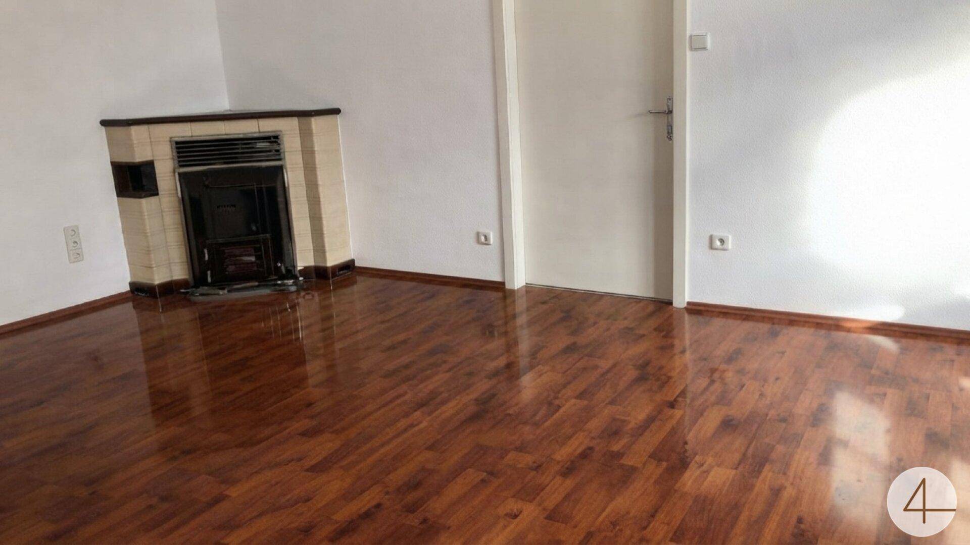 Wohnzimmer mit glänzendem Laminatboden, weißer Tür und einem traditionellen Kaminofen.