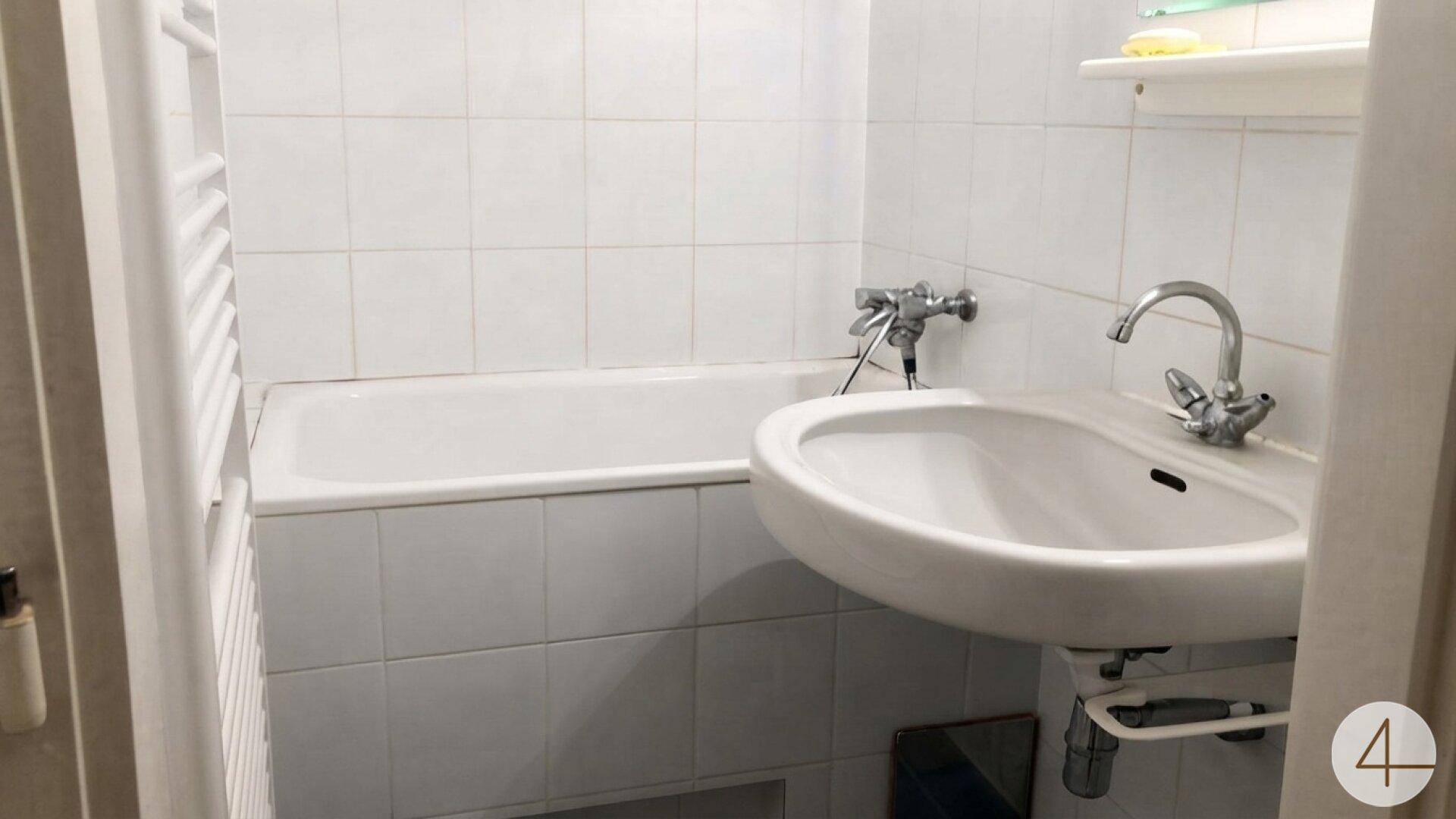 Badezimmer mit weiß gefliesten Wänden, Badewanne, Waschbecken und Handtuchheizkörper.