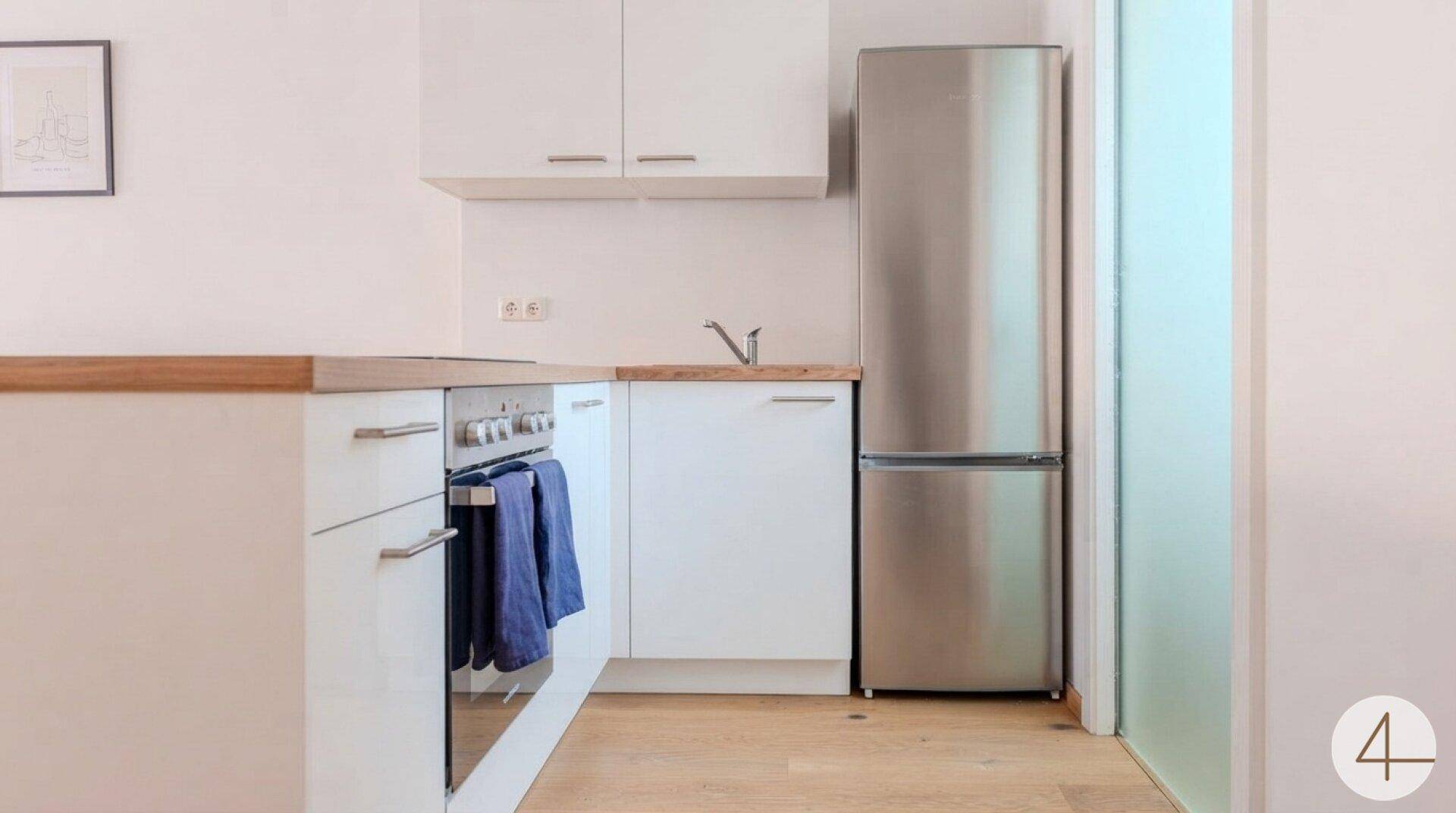Funktionale Küche mit weißen Unterschränken, integriertem Backofen und großem Kühlschrank.