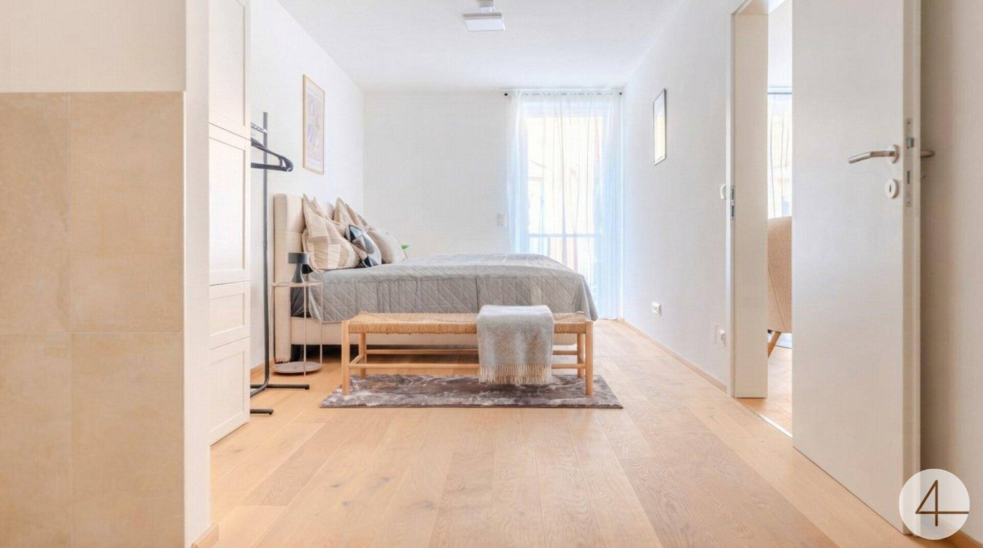 Geräumiges Schlafzimmer mit hellem Holzboden, Doppelbett und Zugang zu einem Balkon.