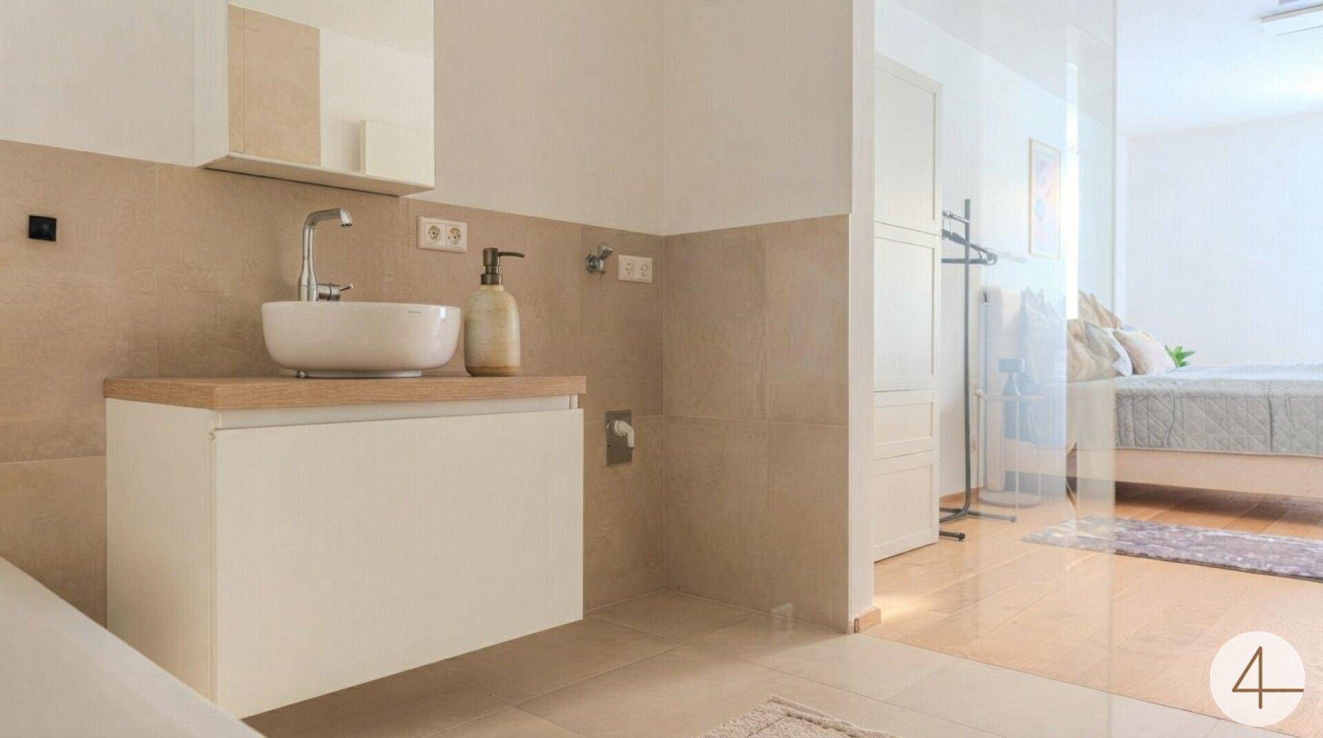 Helles Badezimmer mit modernem Waschtisch, Spiegel und Blick in das angrenzende Schlafzimmer.