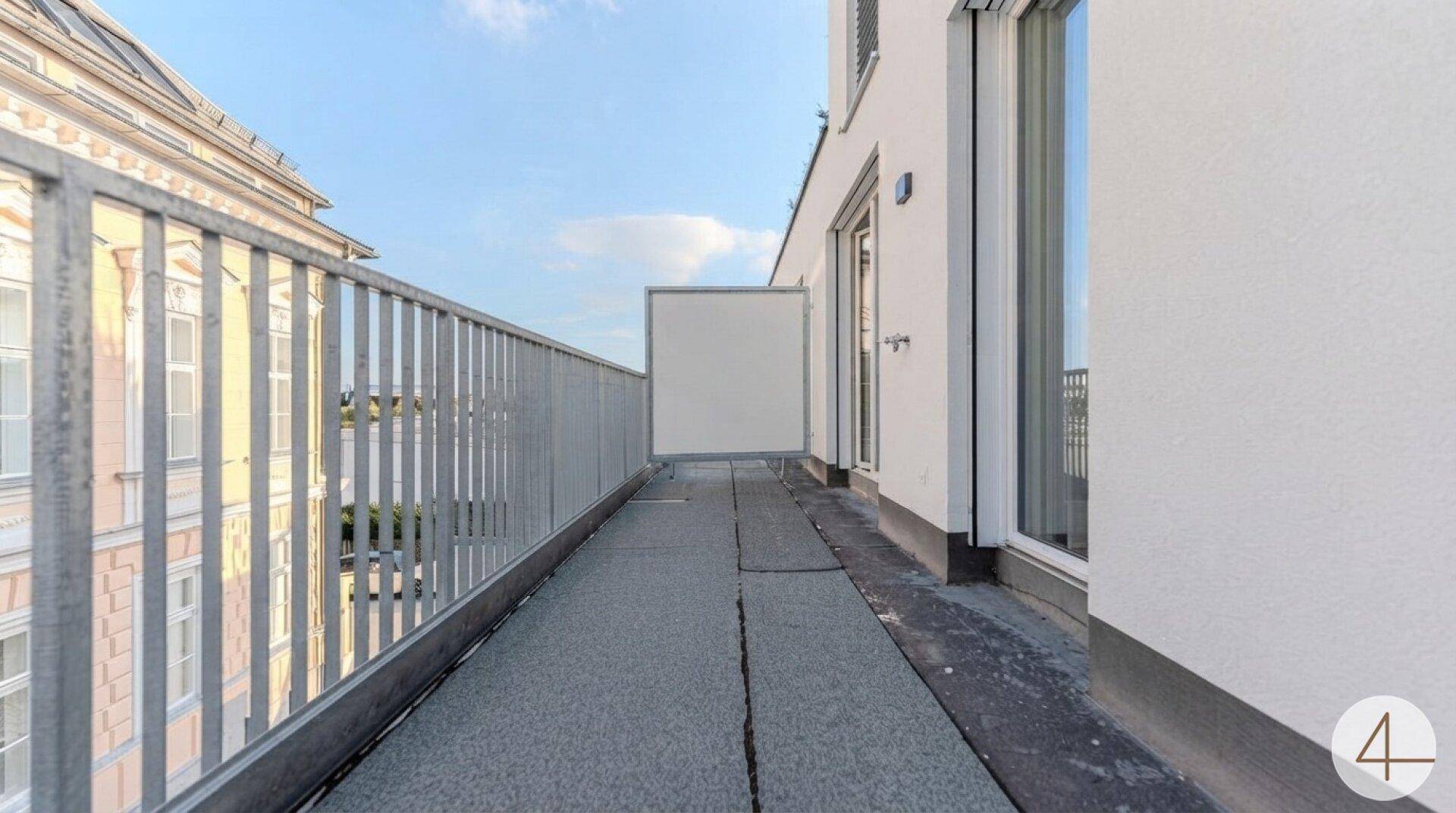 Langer, schmaler Balkon mit Metallgeländer und Blick auf die umliegenden Gebäude.