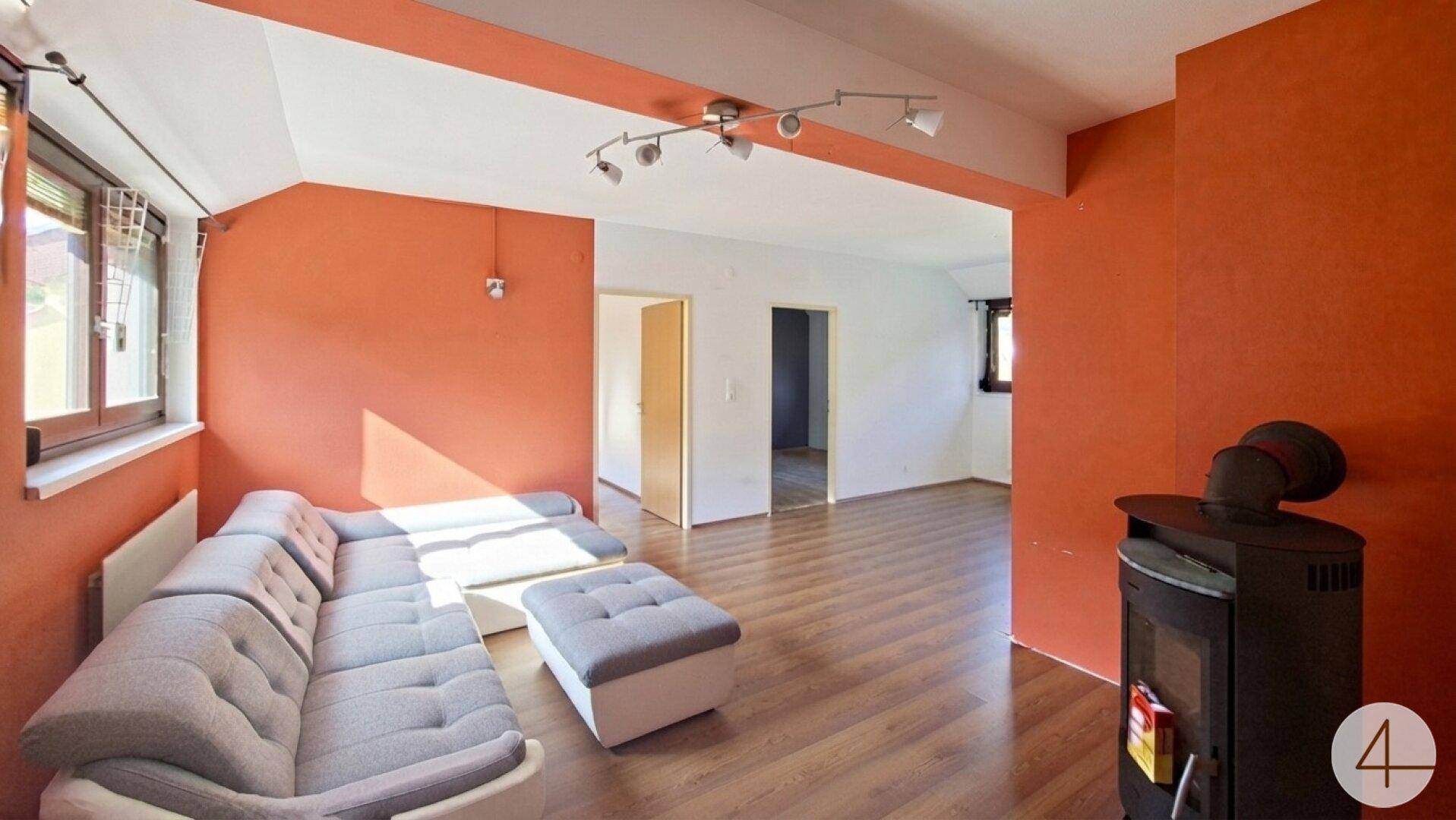 Geräumiges Wohnzimmer mit Holzboden, gemütlichem Sofa und einem stilvollen Holzofen.