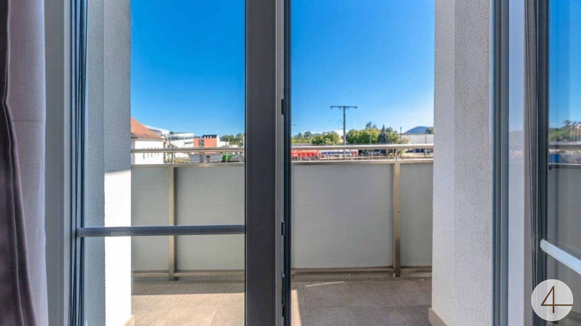 Blick von innen auf einen Balkon mit Metallgeländer und weitem Ausblick.