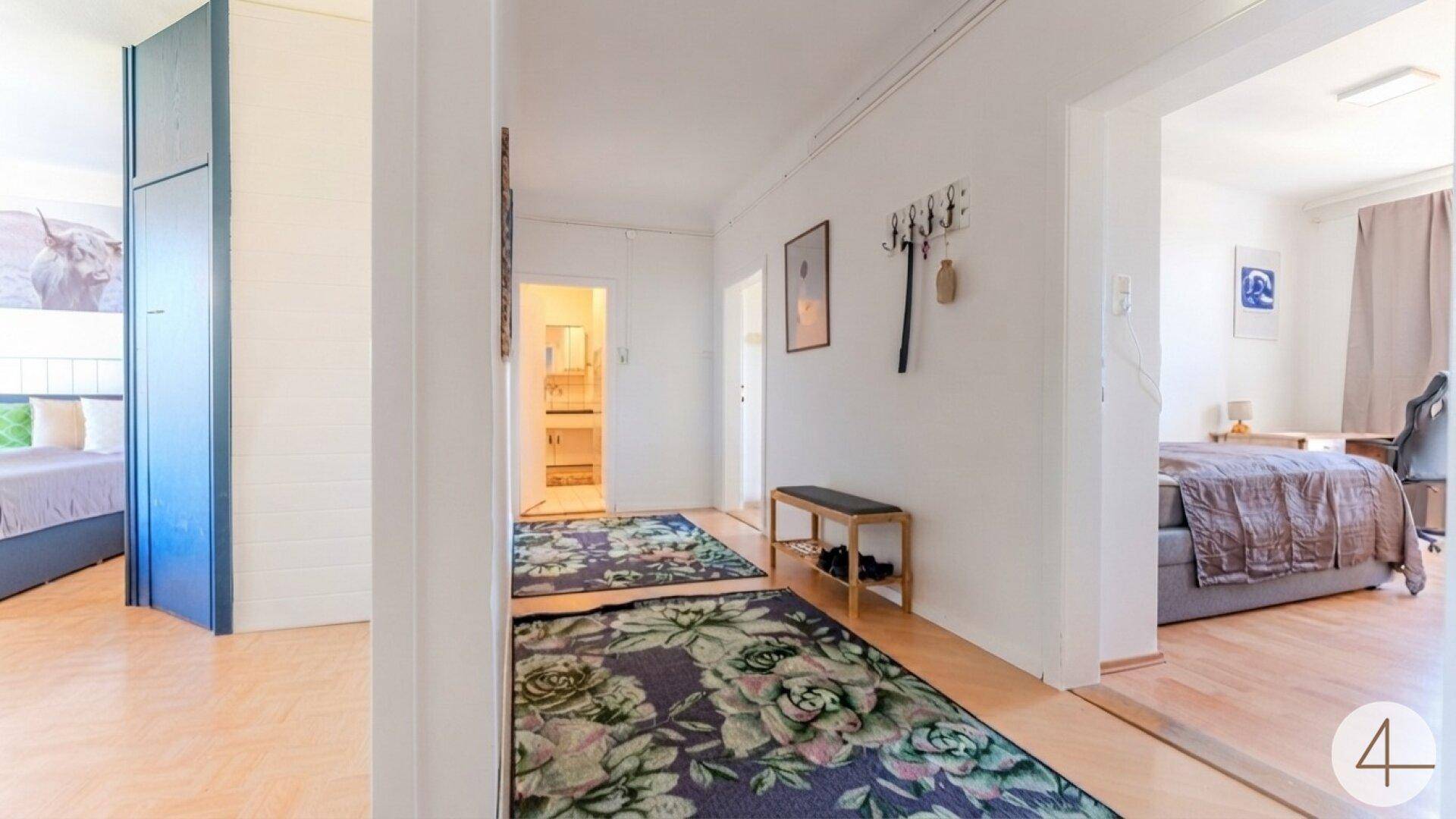 Heller Flur mit Holzfußboden, floralen Teppichen und Zugang zu verschiedenen Zimmern.