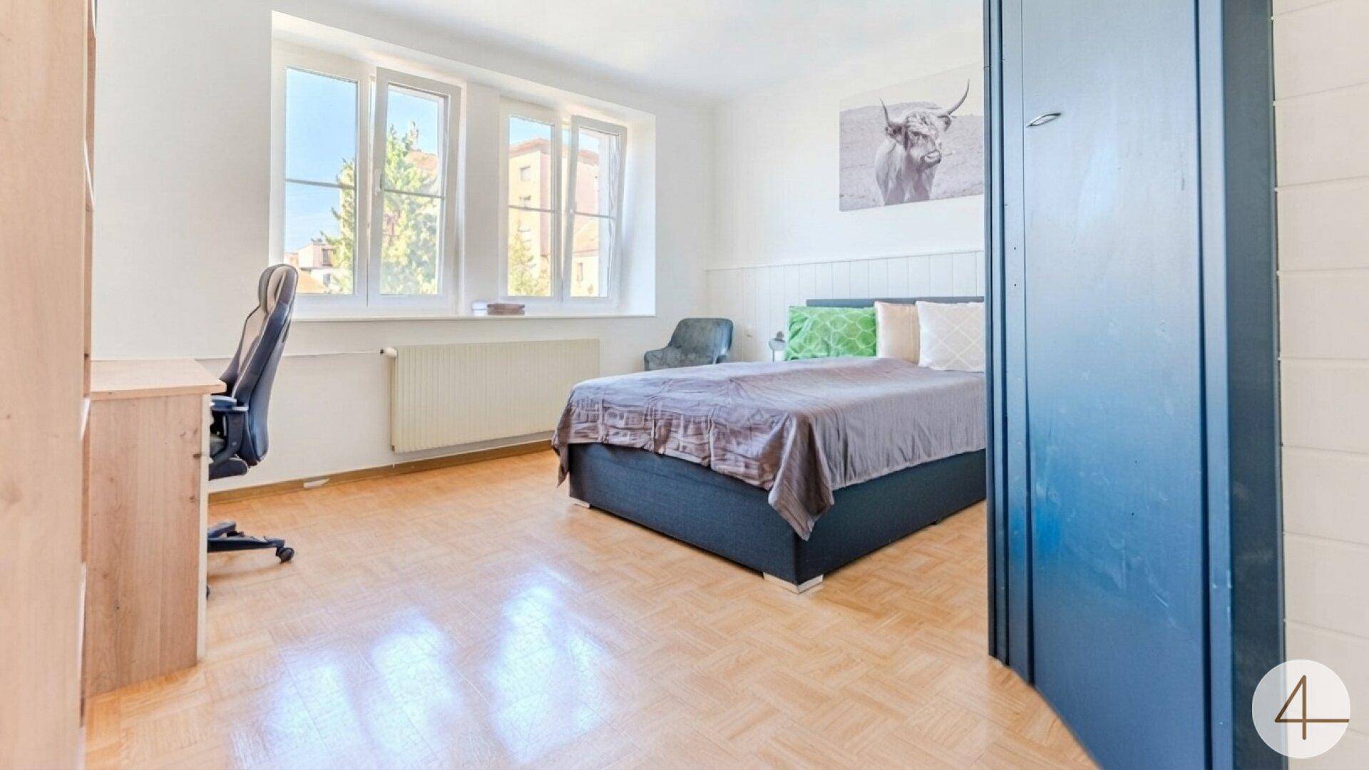 Geräumiges Schlafzimmer mit Bett, Schreibtisch und drei großen Fenstern.