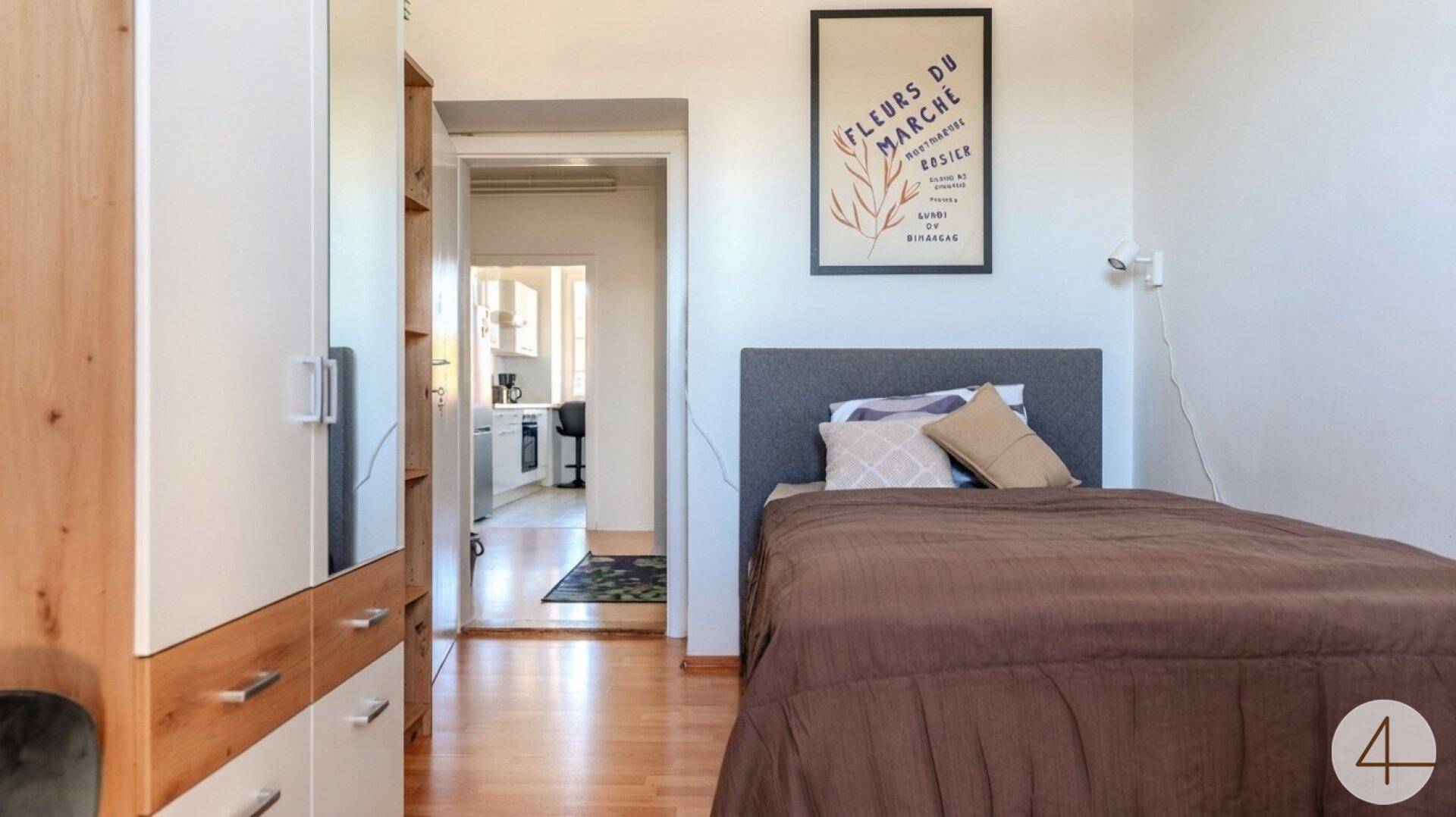 Schlafzimmer mit Bett und Kleiderschrank, mit Blick in den Flur und die Küche.