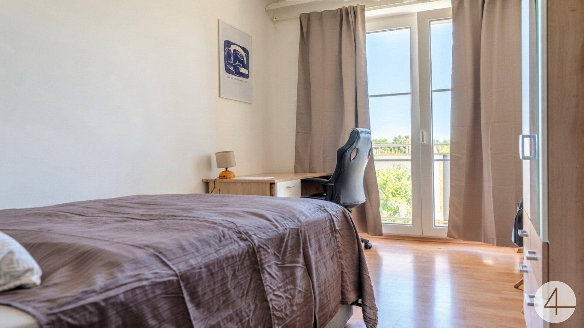 Schlafzimmer mit Bett, Schreibtisch und Zugang zu einem Balkon.