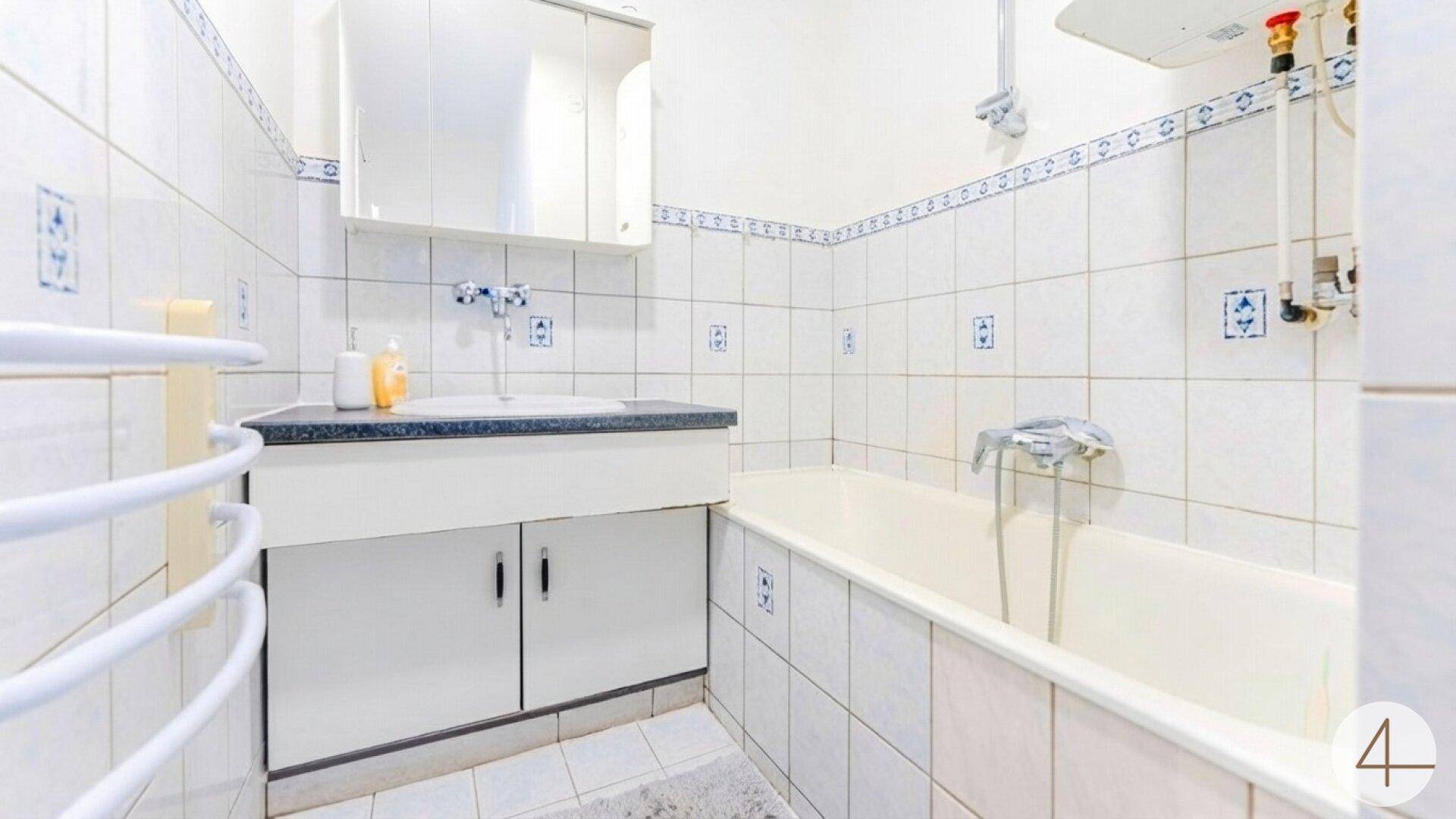 Badezimmer mit Badewanne, Waschbecken, Spiegelschrank und Handtuchheizkörper.