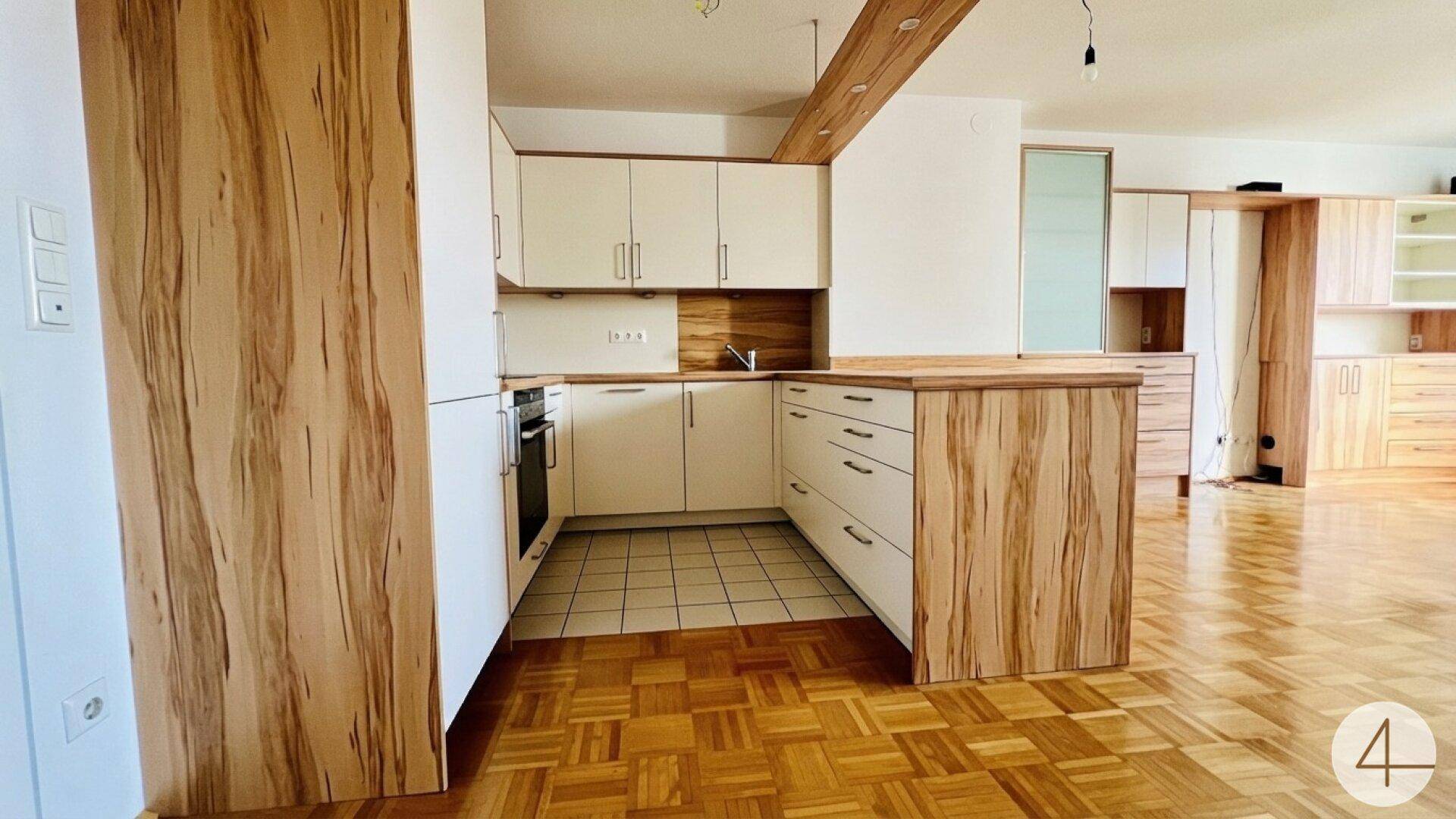 Funktionale Einbauküche mit hellen Fronten und Holzdetails, offen zum Wohnbereich.